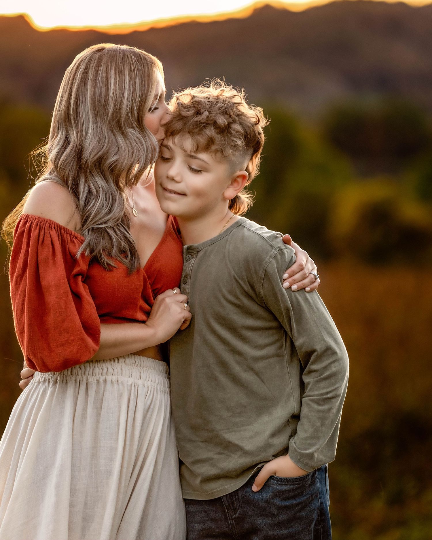 Mother hugging son and kissing the side of his head during golden hour in central NY