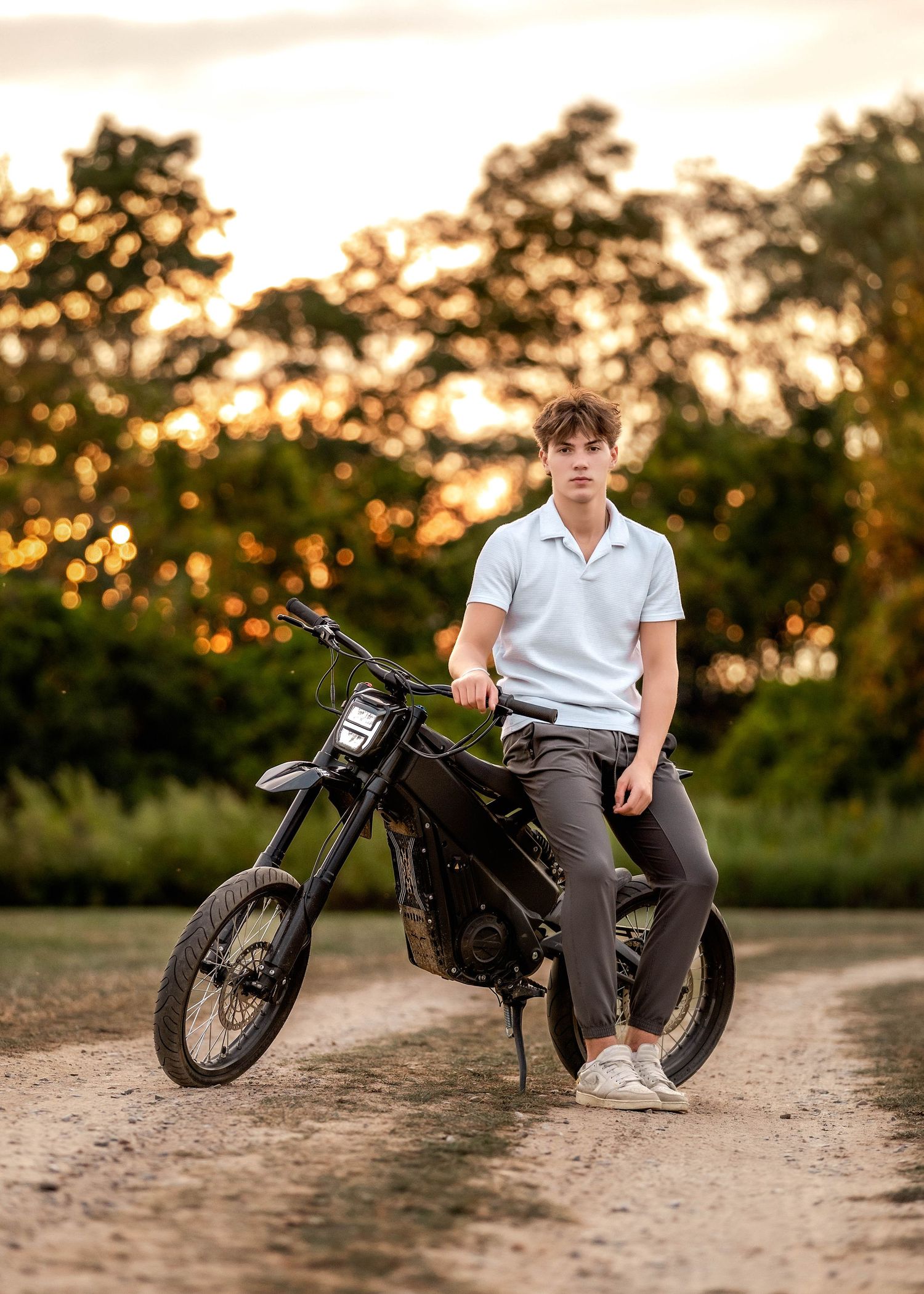 Senior boy leaning against a dirt bike with a sunset background in central NY