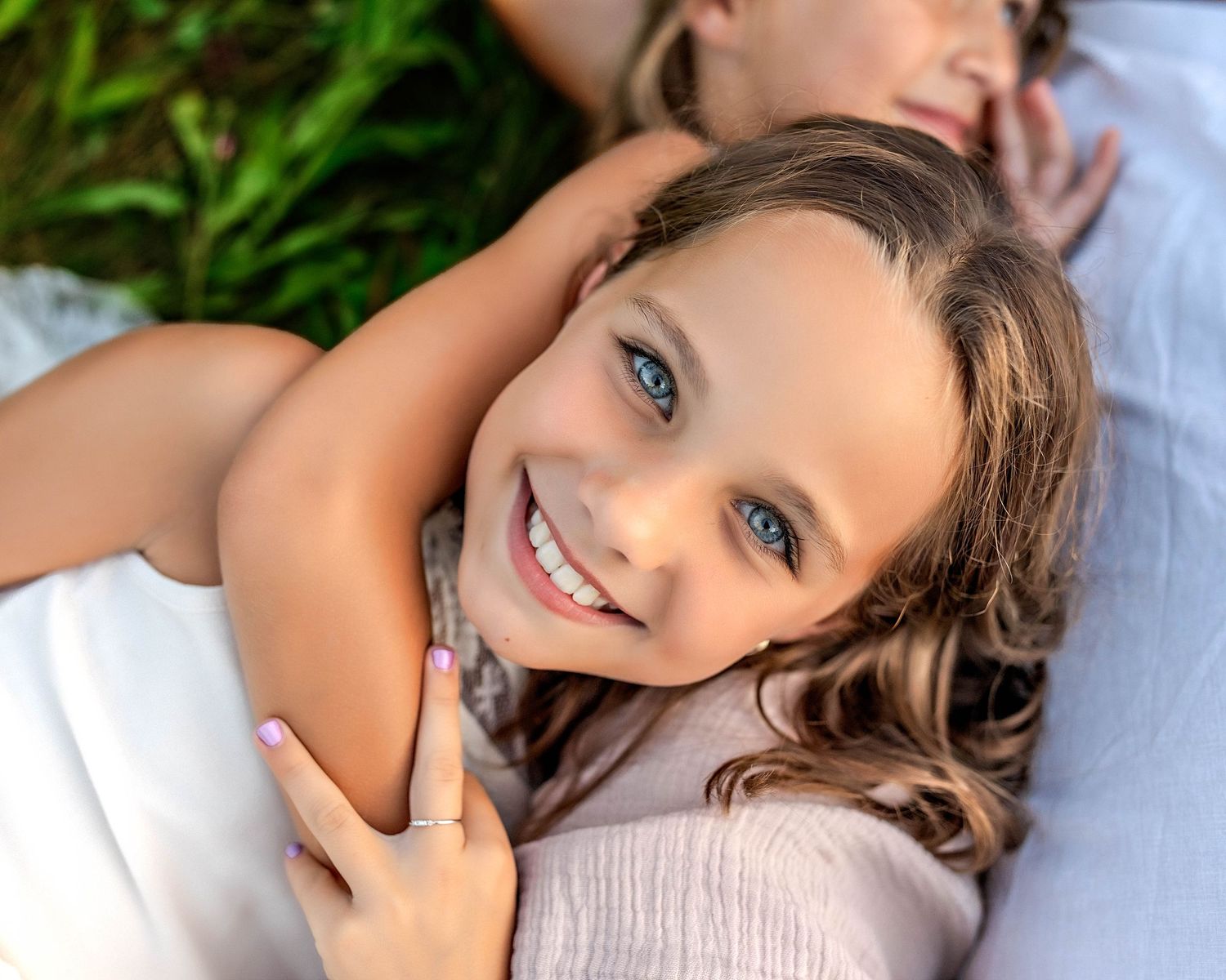 Blue eyed little girl laying on sister looking up at the camera