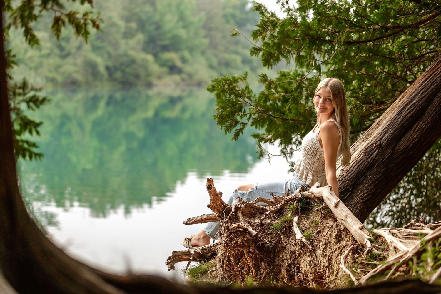 Senior girl sitting on a tree stump in front of a lake in Central NY