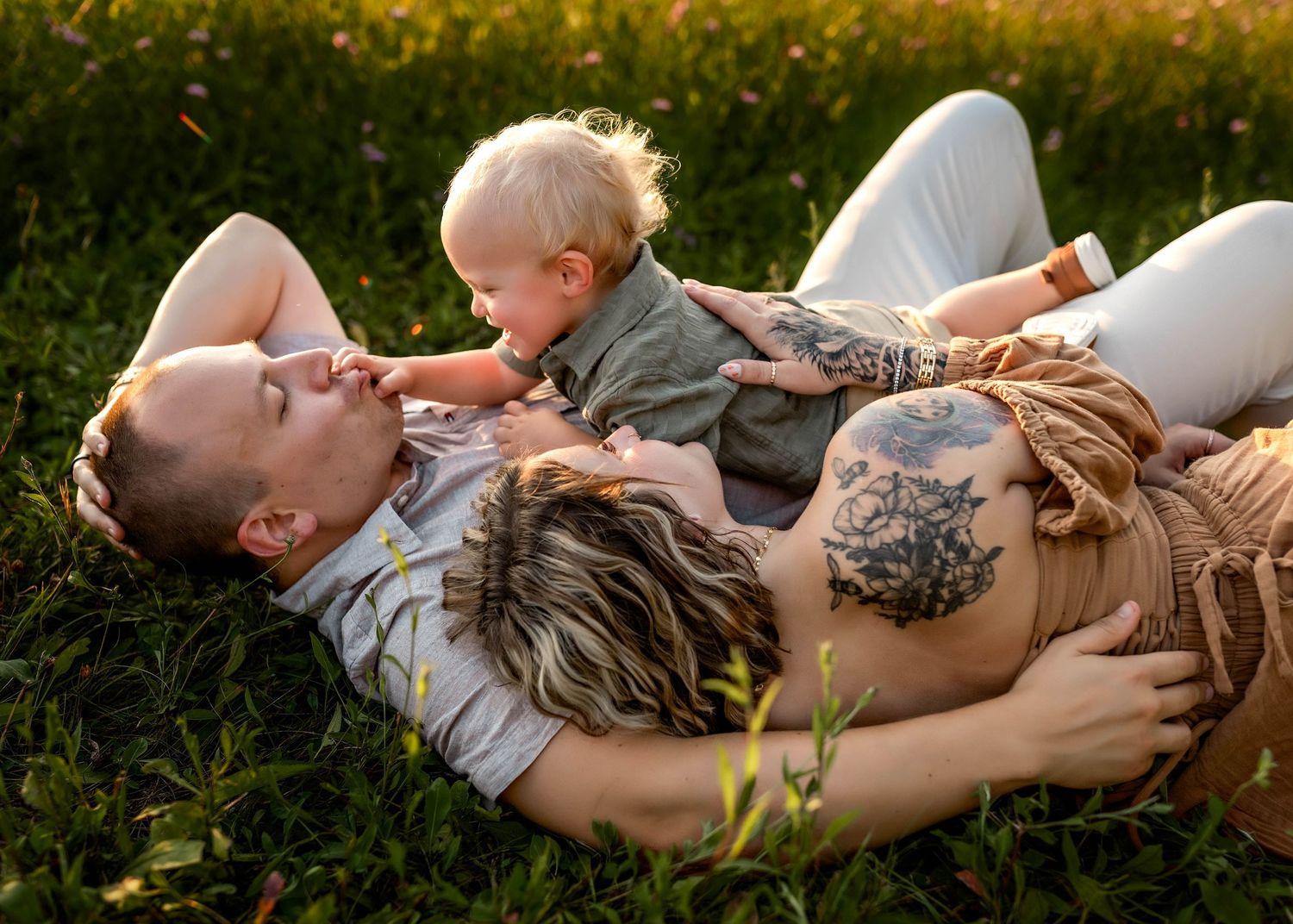 Parents laying in the grass with their toddler cuddling them in Central NY