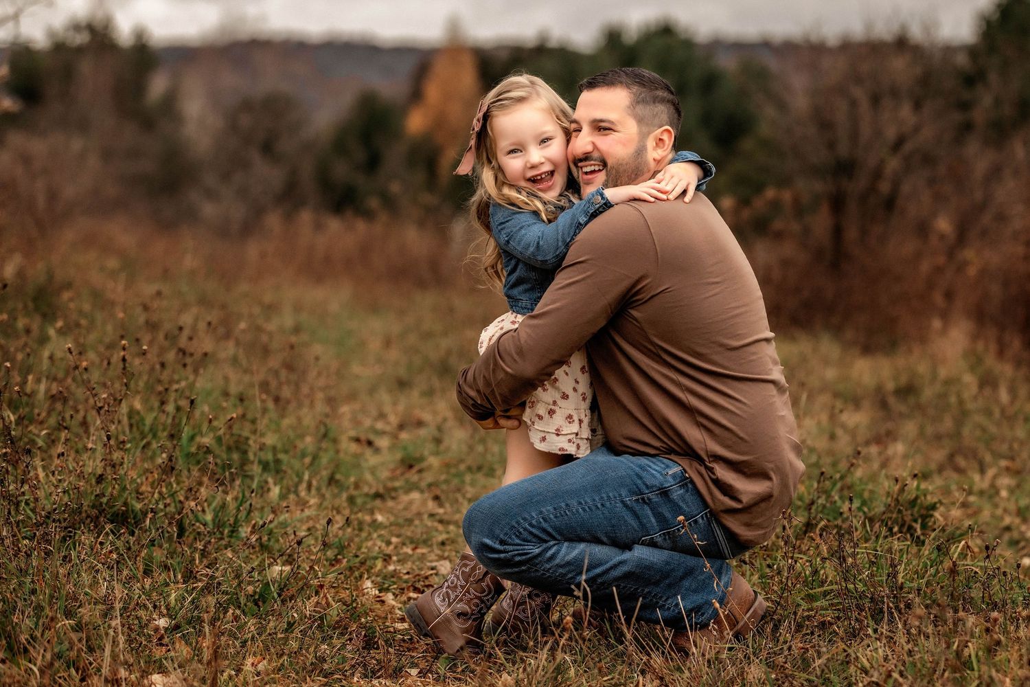 Daughter hugging father while he squats down in a field in the fall