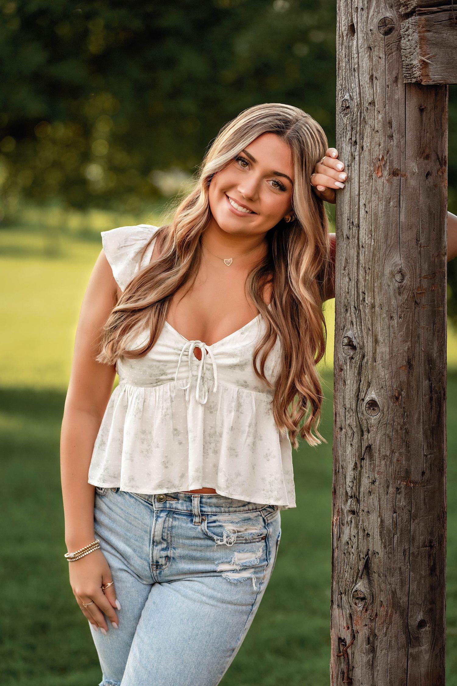 Senior girl leaning against a wood post in a country setting