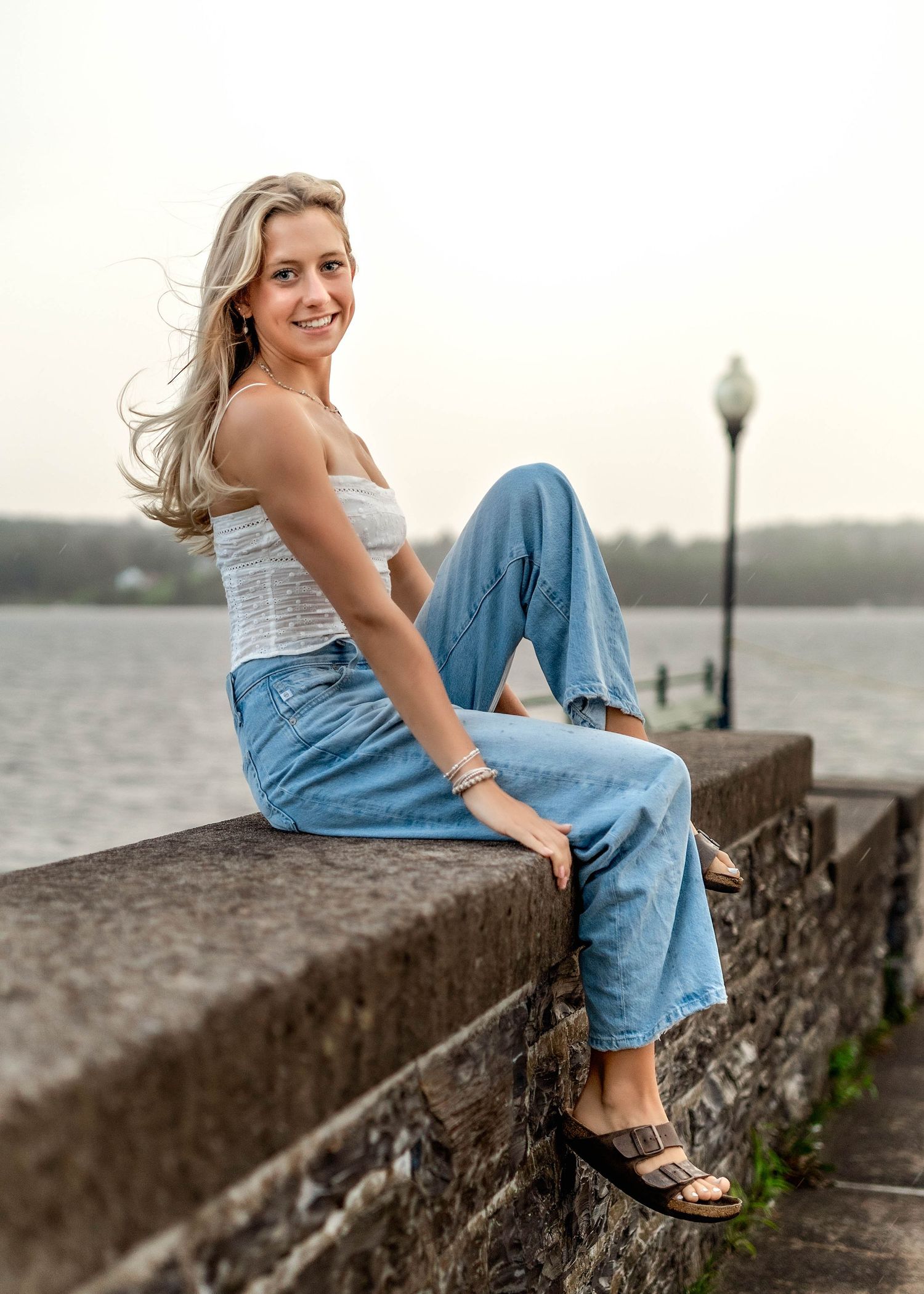 Senior girl sitting on a sea wall in front of a lake in central NY