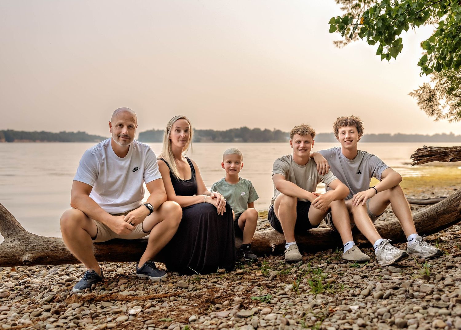 Family sitting on a fallen tree in front of a lake during sunset in Central NY