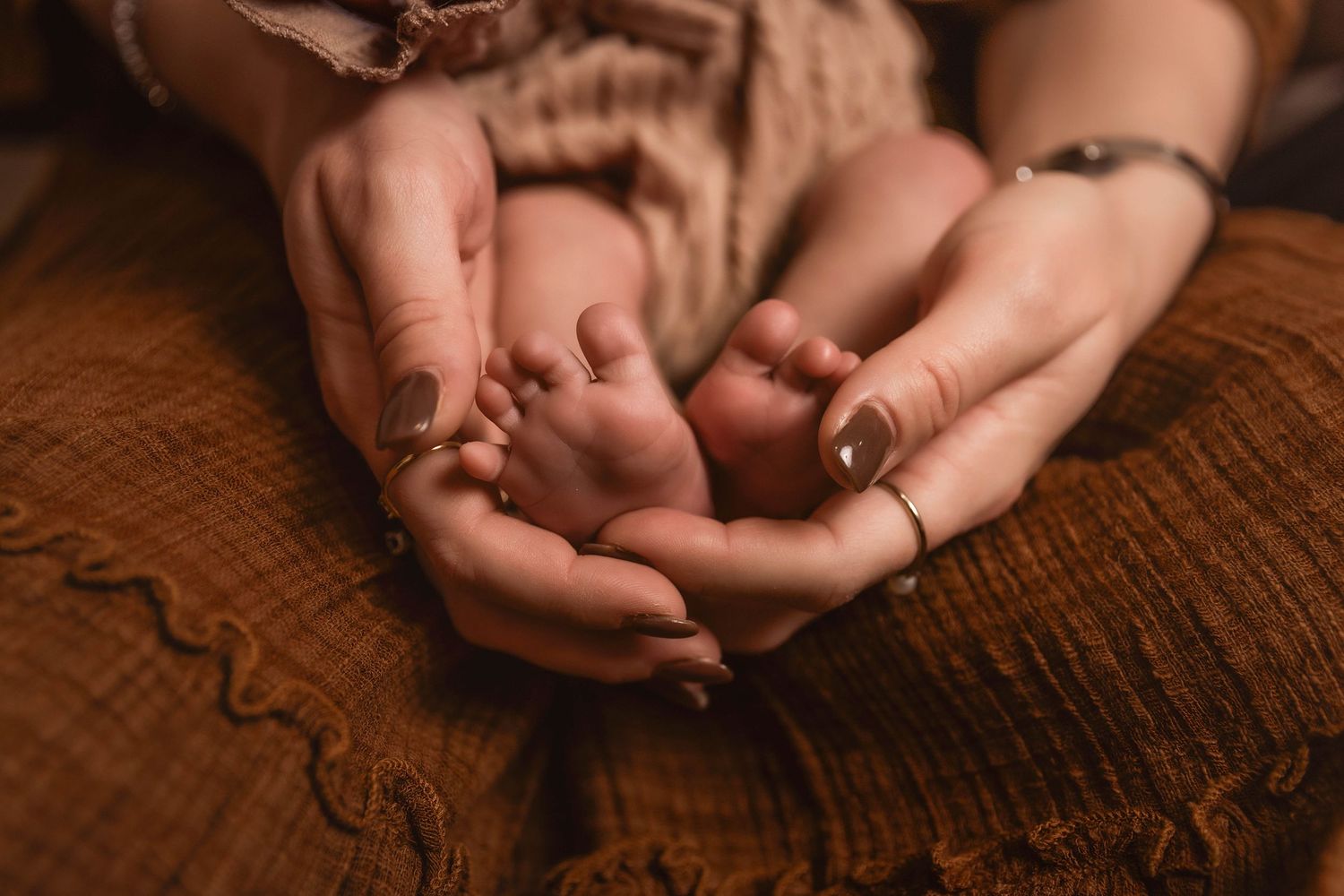 Mother cradling newborn baby's feet in her hands resting on her lap during lifestyle newborn photos in Central NY