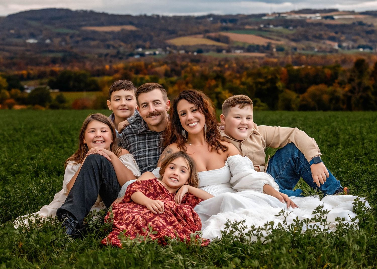 Family of 6 sitting on the ground huddled together for family photo in a field in Central NY