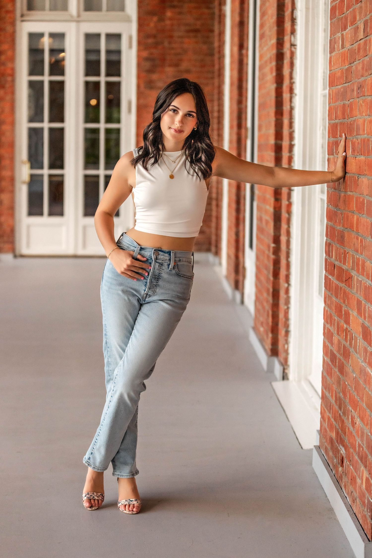 Senior girl leaning against a brick wall with jeans and high heels in Central NY