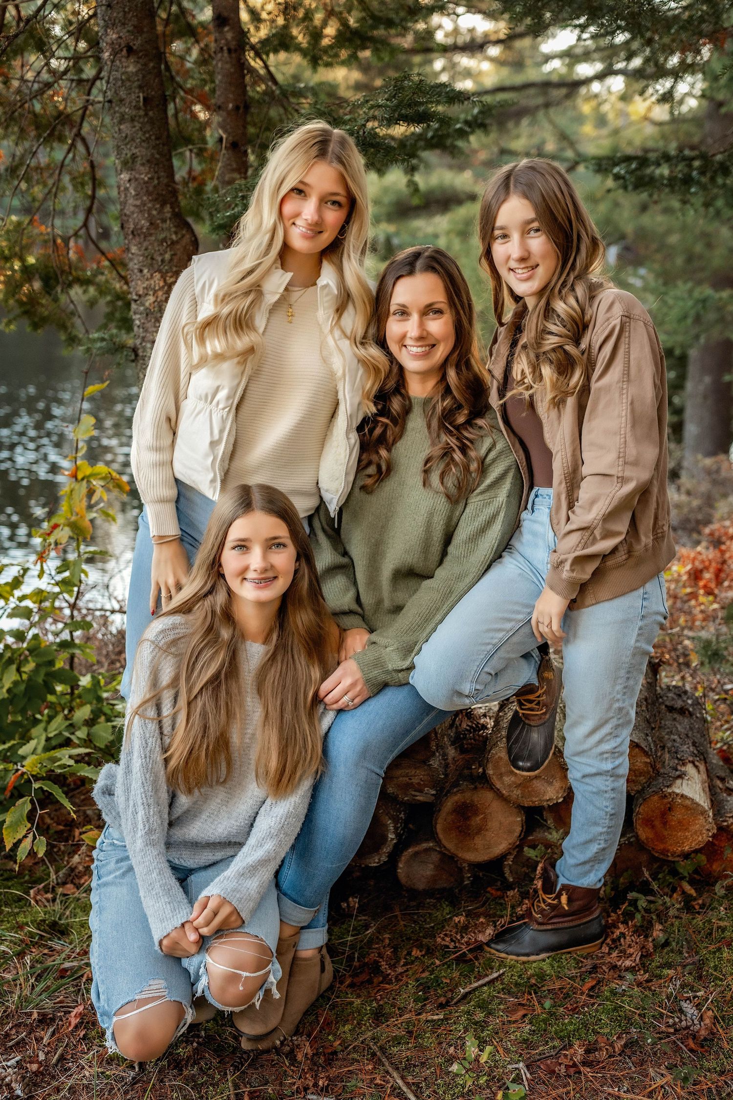 Mom and daughters sitting together on a wood pile in the fall by the pond