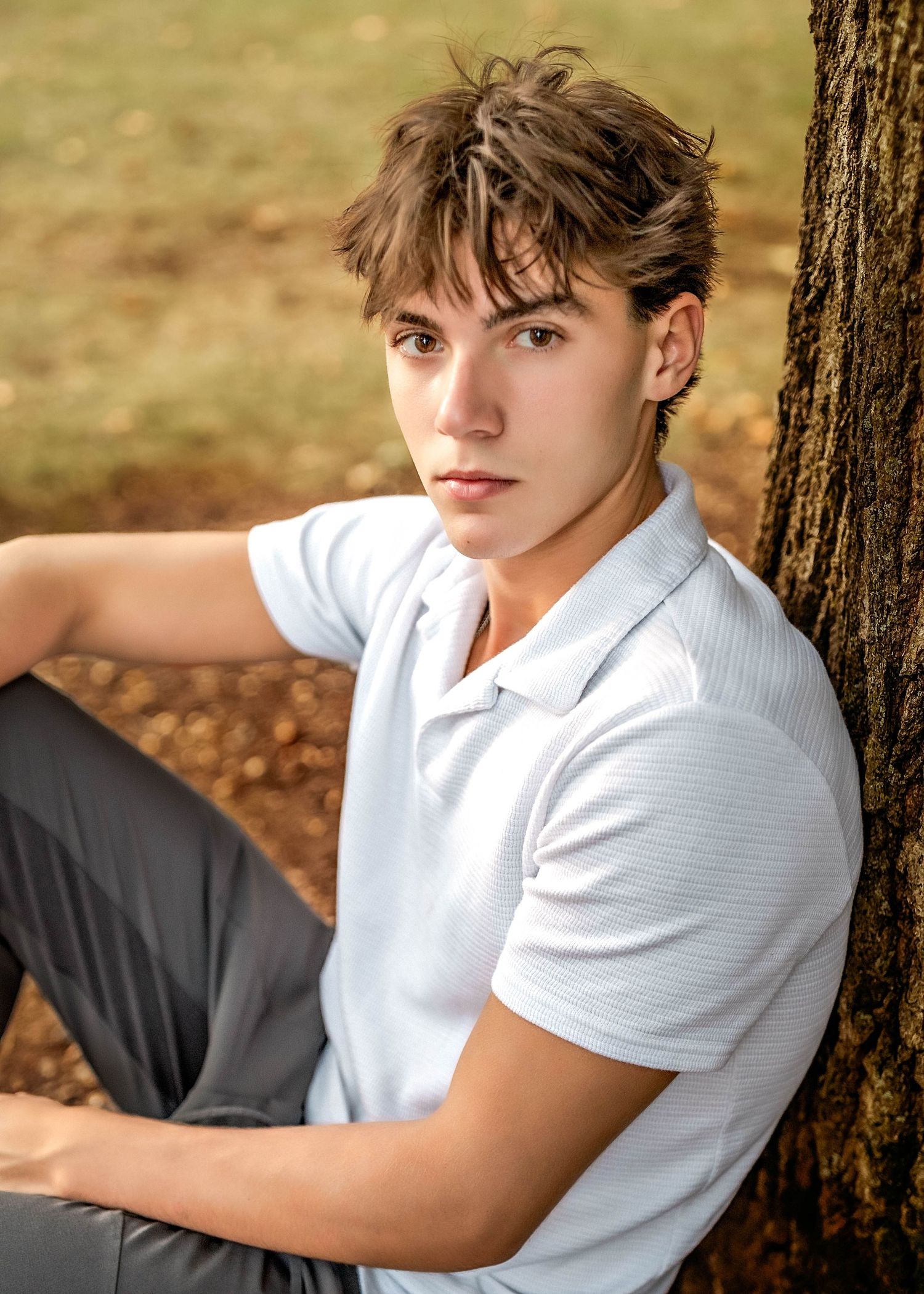 Senior boy sitting on the ground leaning against a tree in central NY