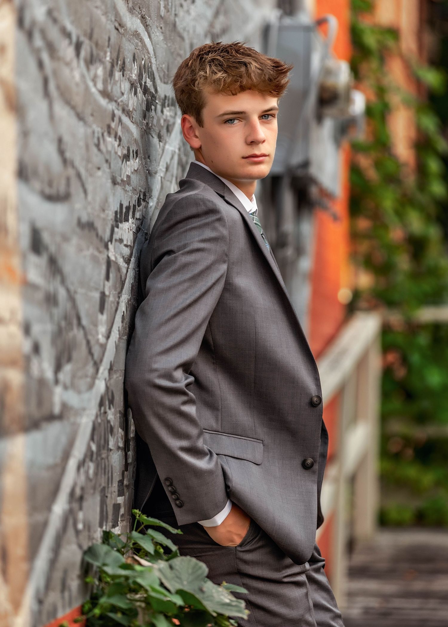 Senior boy leaning against a stone wall with suit on
