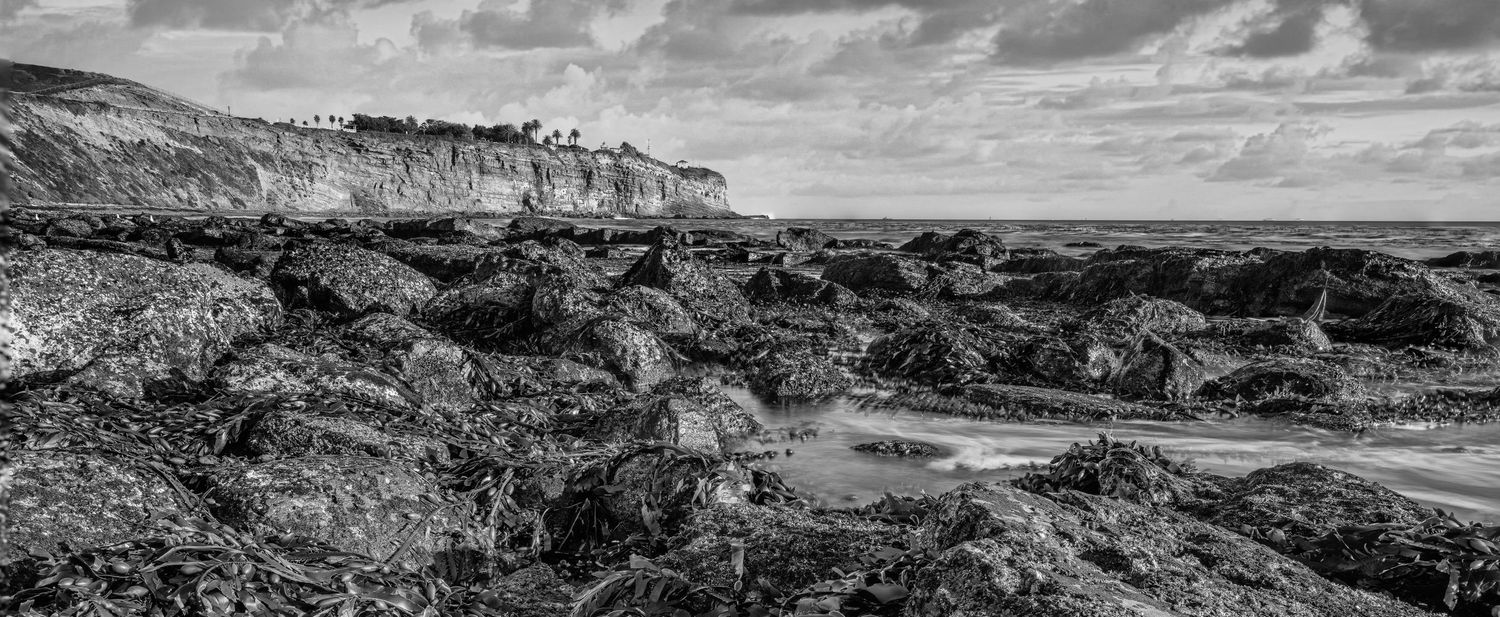 Wide panoramic black and white landscape of rocky coastal cliffs and rugged terrain.