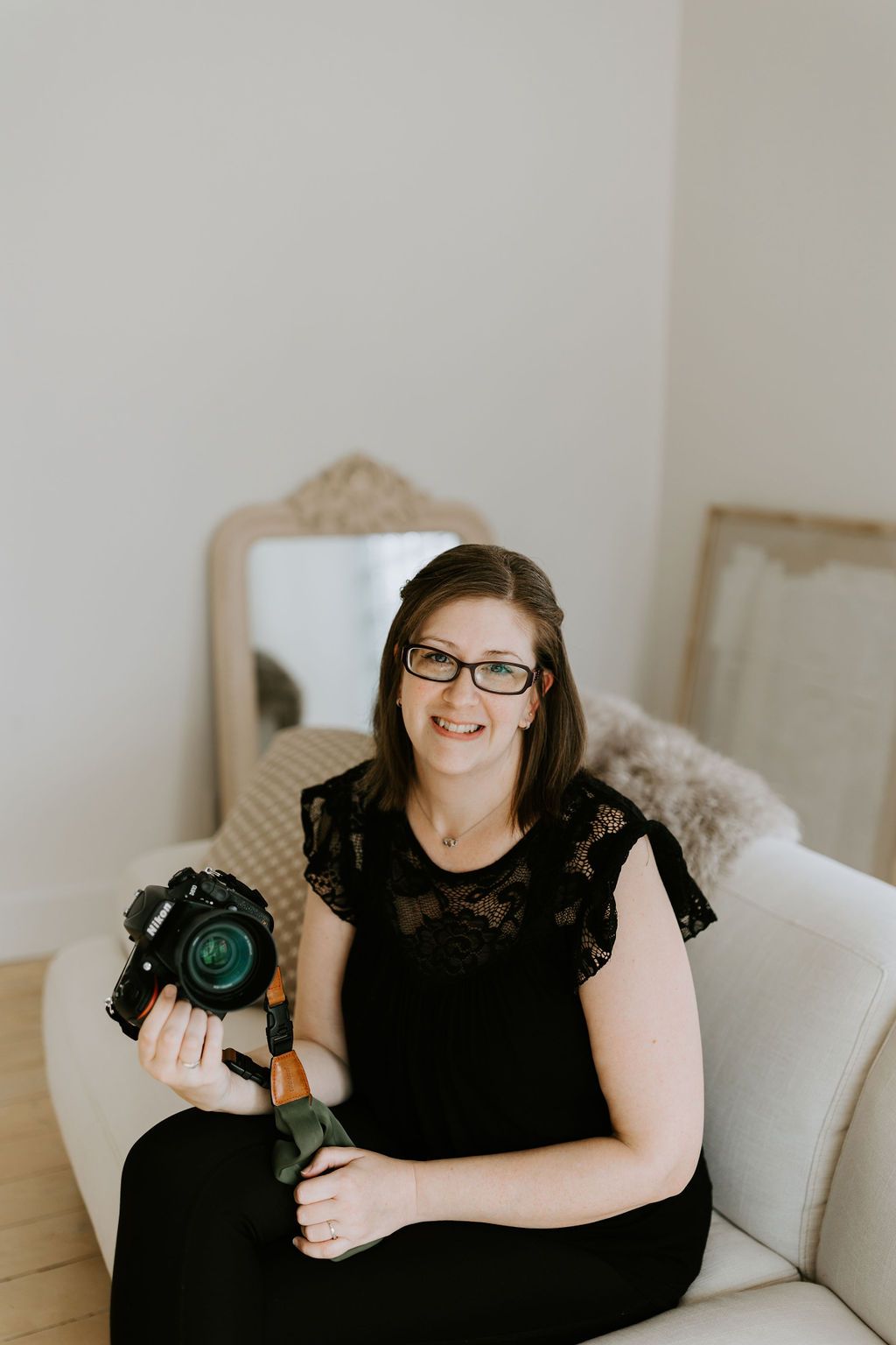 A photo of Kari Mills from Kari Mills Photography, posing with her camera in a studio. Kari has a Nikon camera.