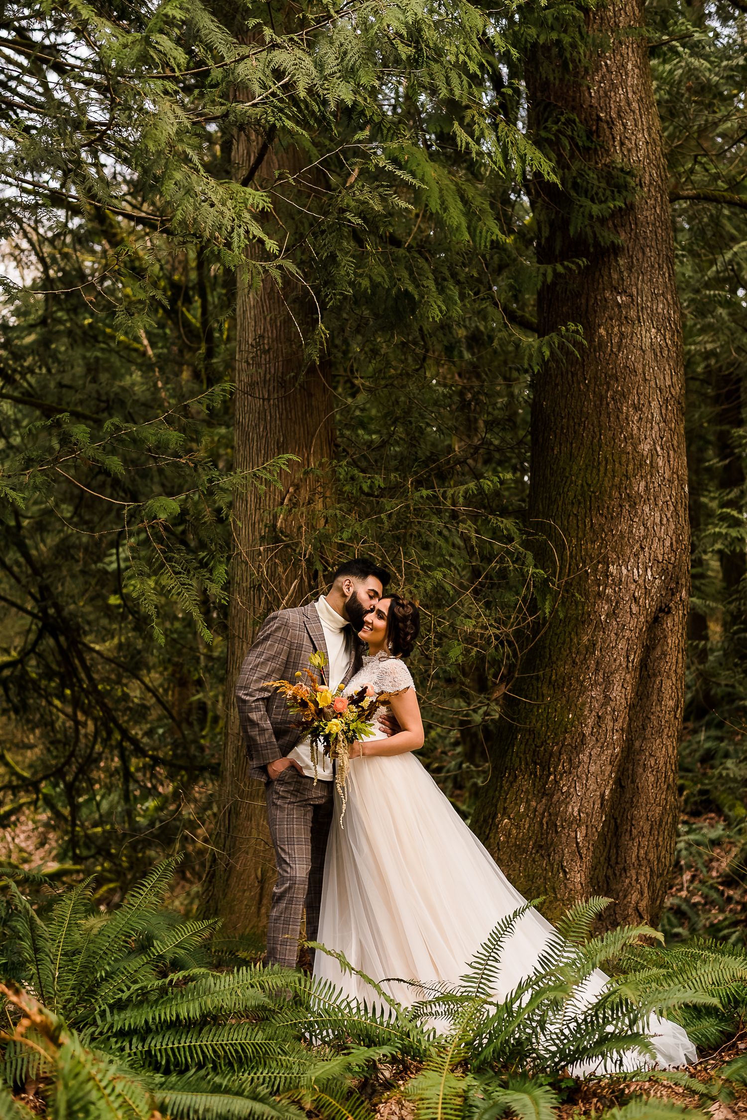 A groom kisses his bride on the cheek in a magical pacific northwest forest.