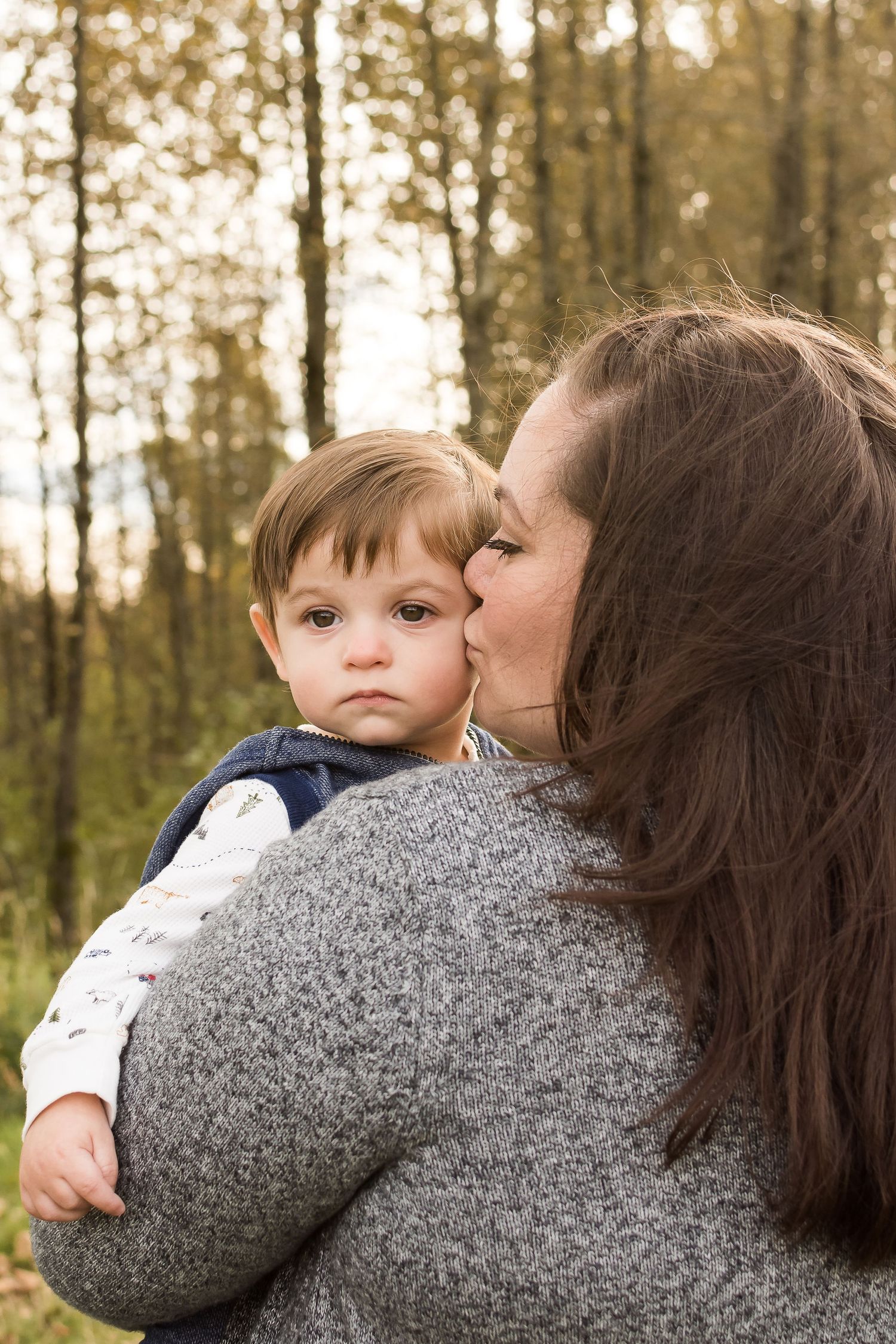 During an autumn afternoon, a mother lovingly kisses her young son on the cheek.