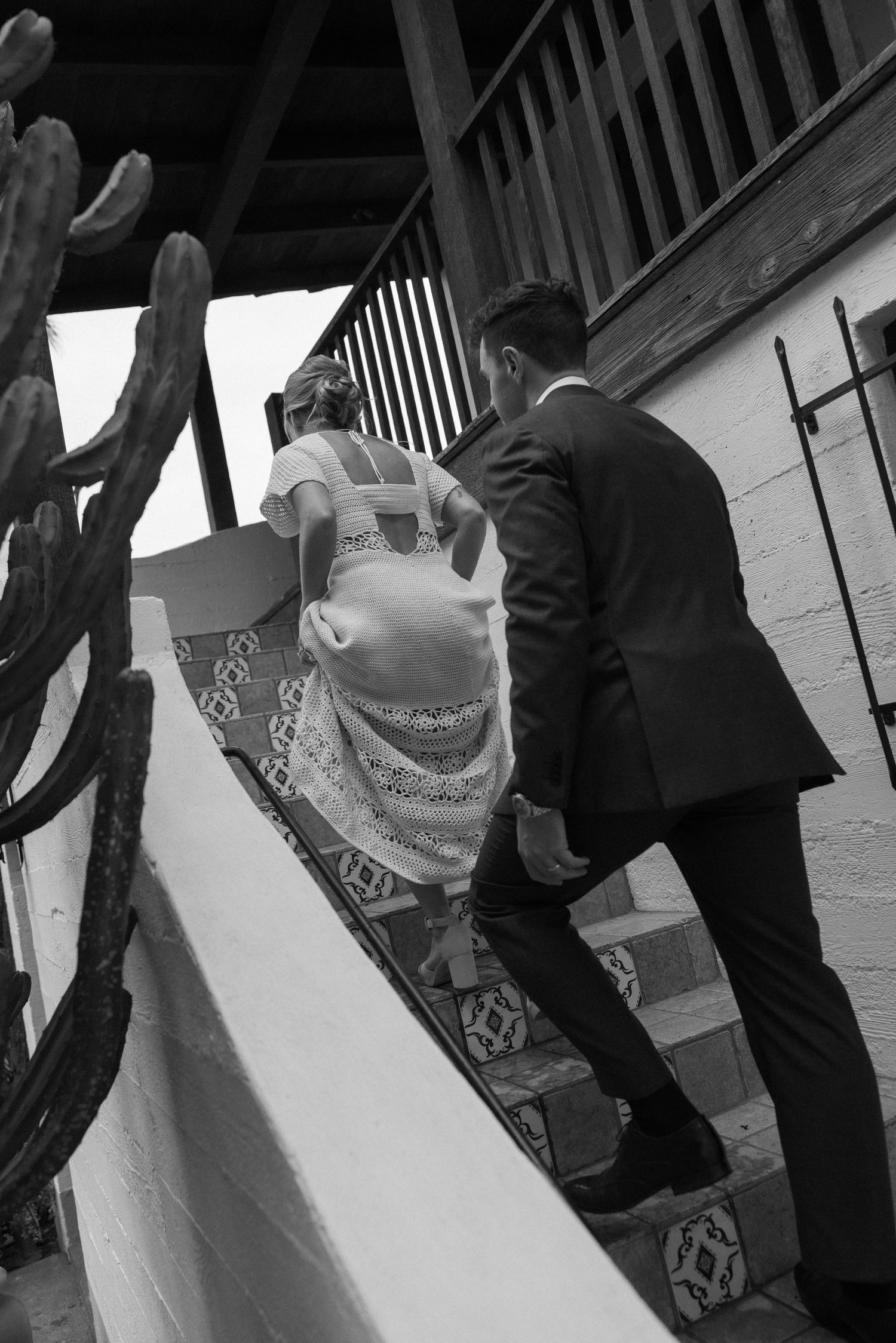 Black and white photo of a bride and groom ascending tiled stairs at a wedding venue.