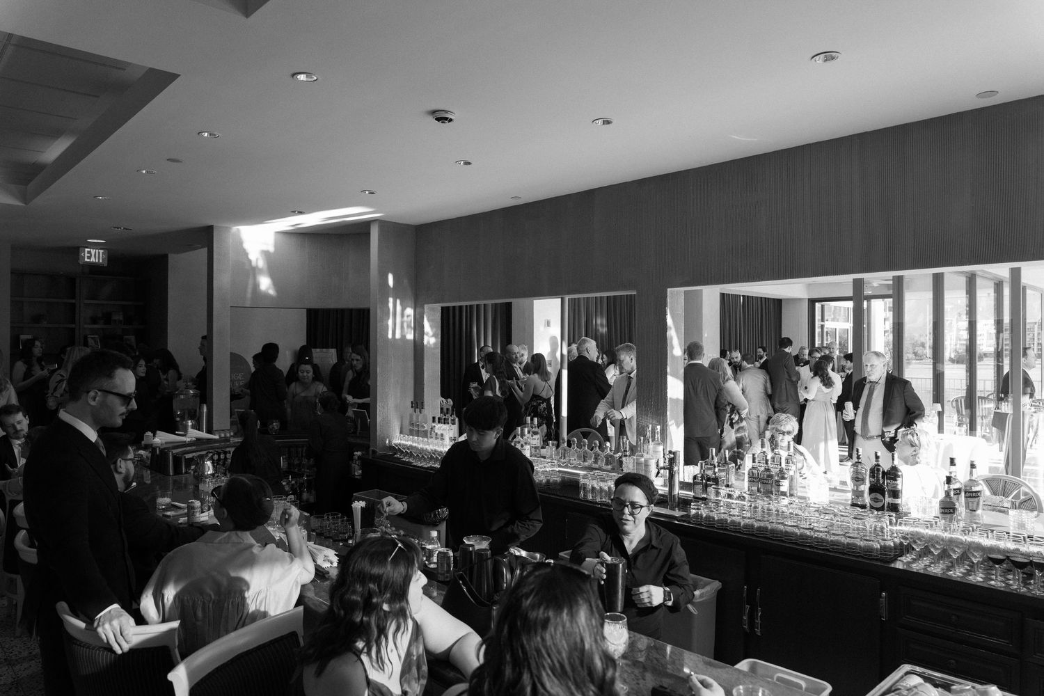 Black and white photo of a busy upscale bar with guests socializing and bartenders serving drinks.