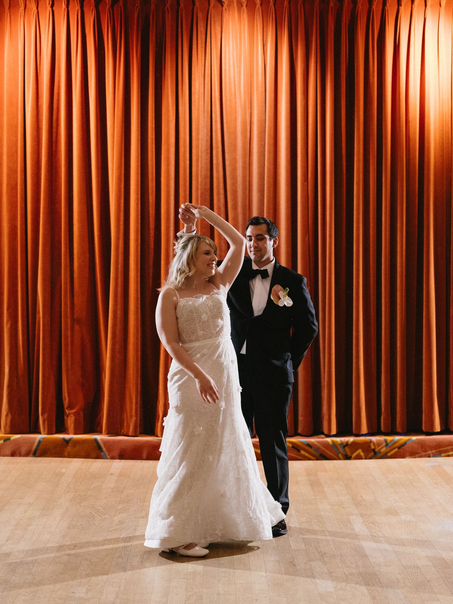 Bride and groom share their first dance in front of elegant orange curtains at their wedding reception.