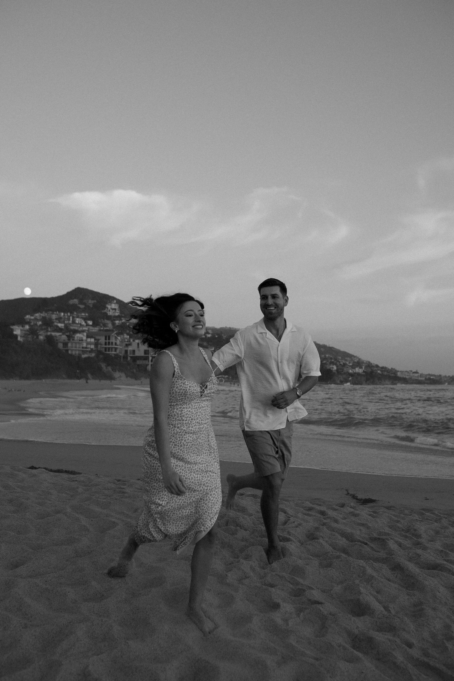 A couple running joyfully on a beach at sunset in black and white.
