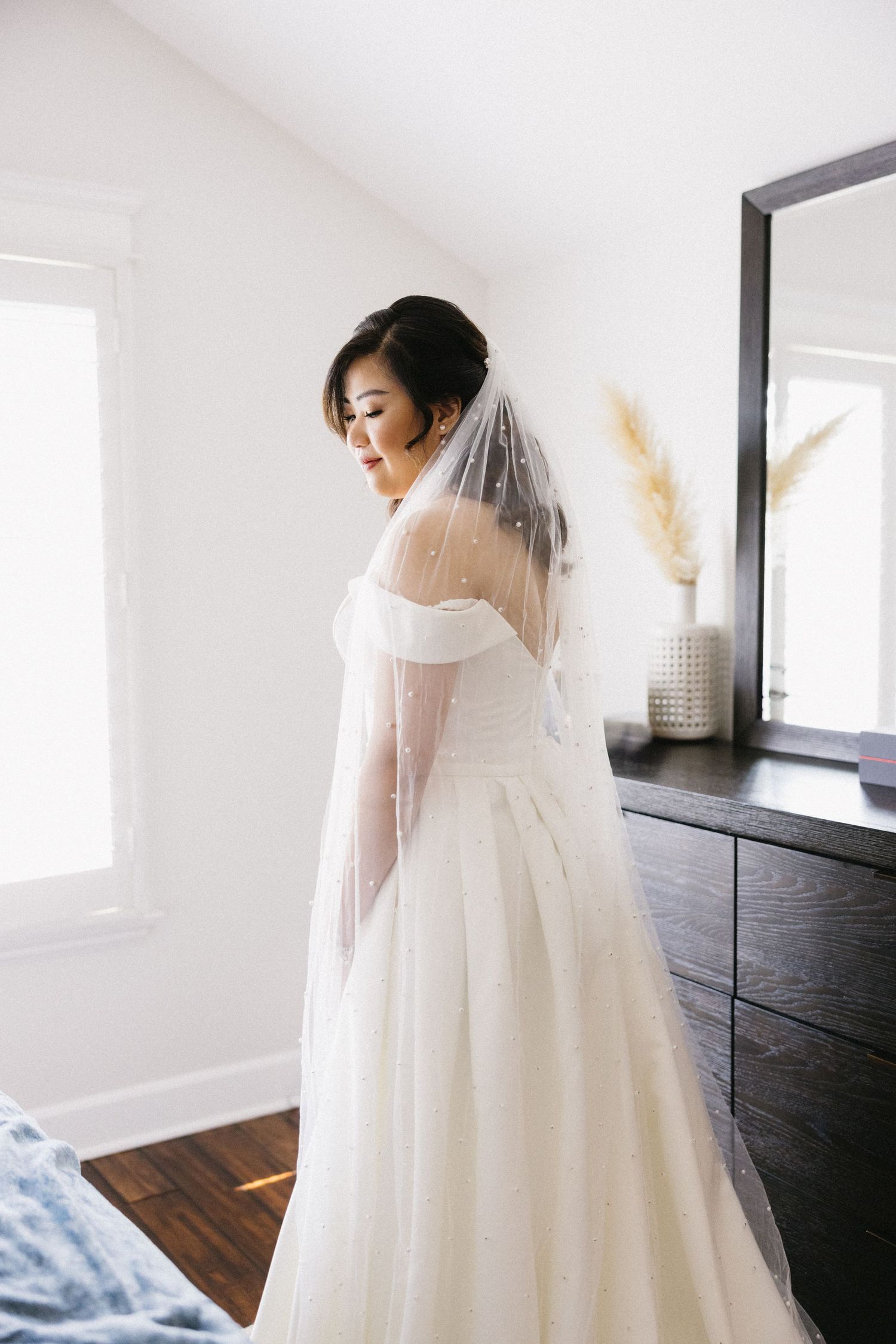 Elegant white wedding dress with flowing veil captured in minimalist interior setting.