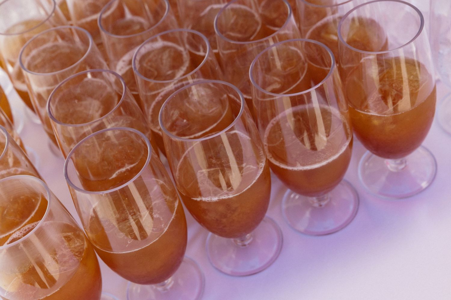 Rows of elegant stemmed glasses filled with a golden amber beverage arranged neatly on a white surface.