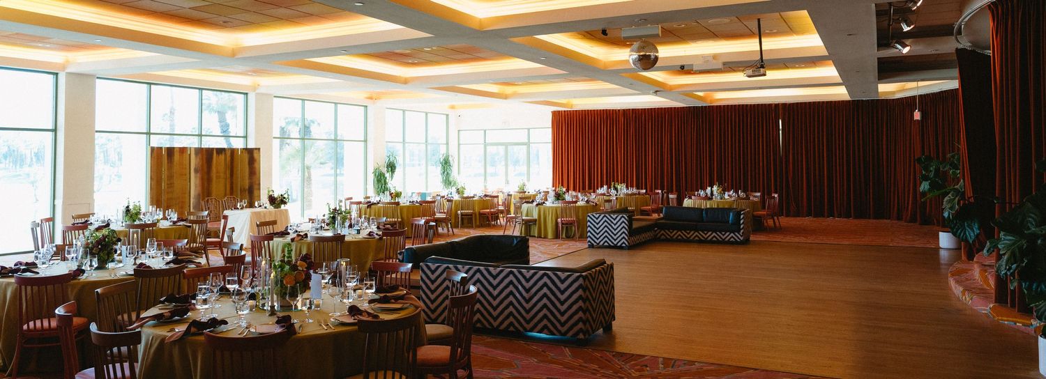 Elegant banquet hall with round tables, warm lighting, wood paneling, and large windows for a sophisticated event.