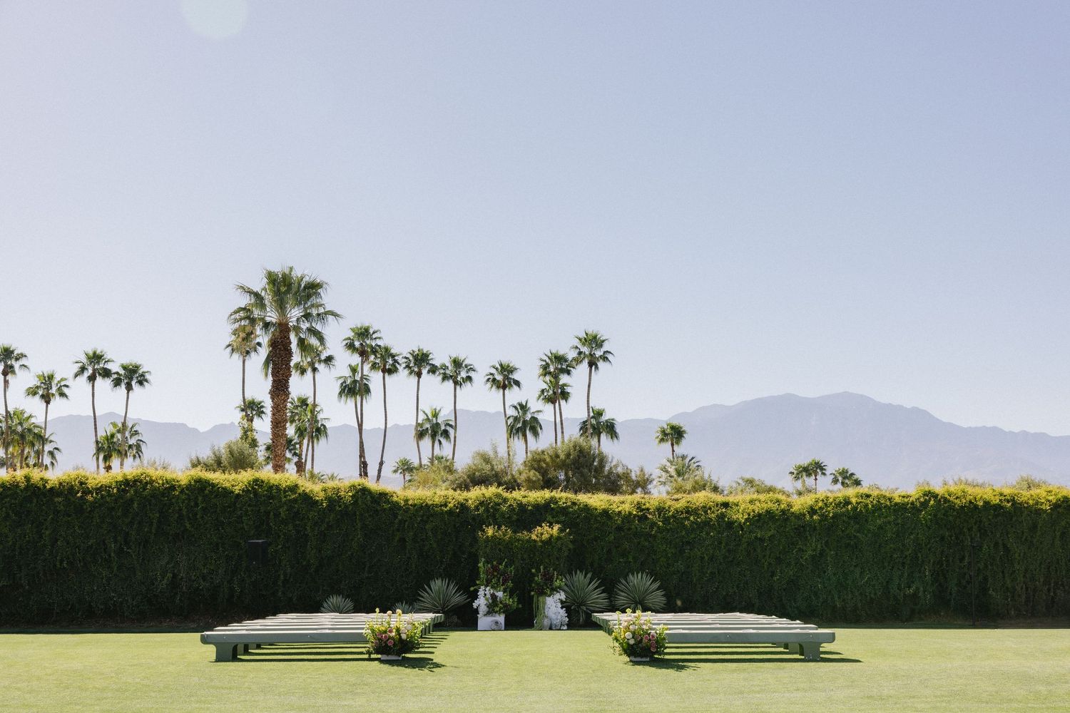 Outdoor wedding ceremony setup on lush green lawn with palm trees and mountain backdrop in Palm Springs.