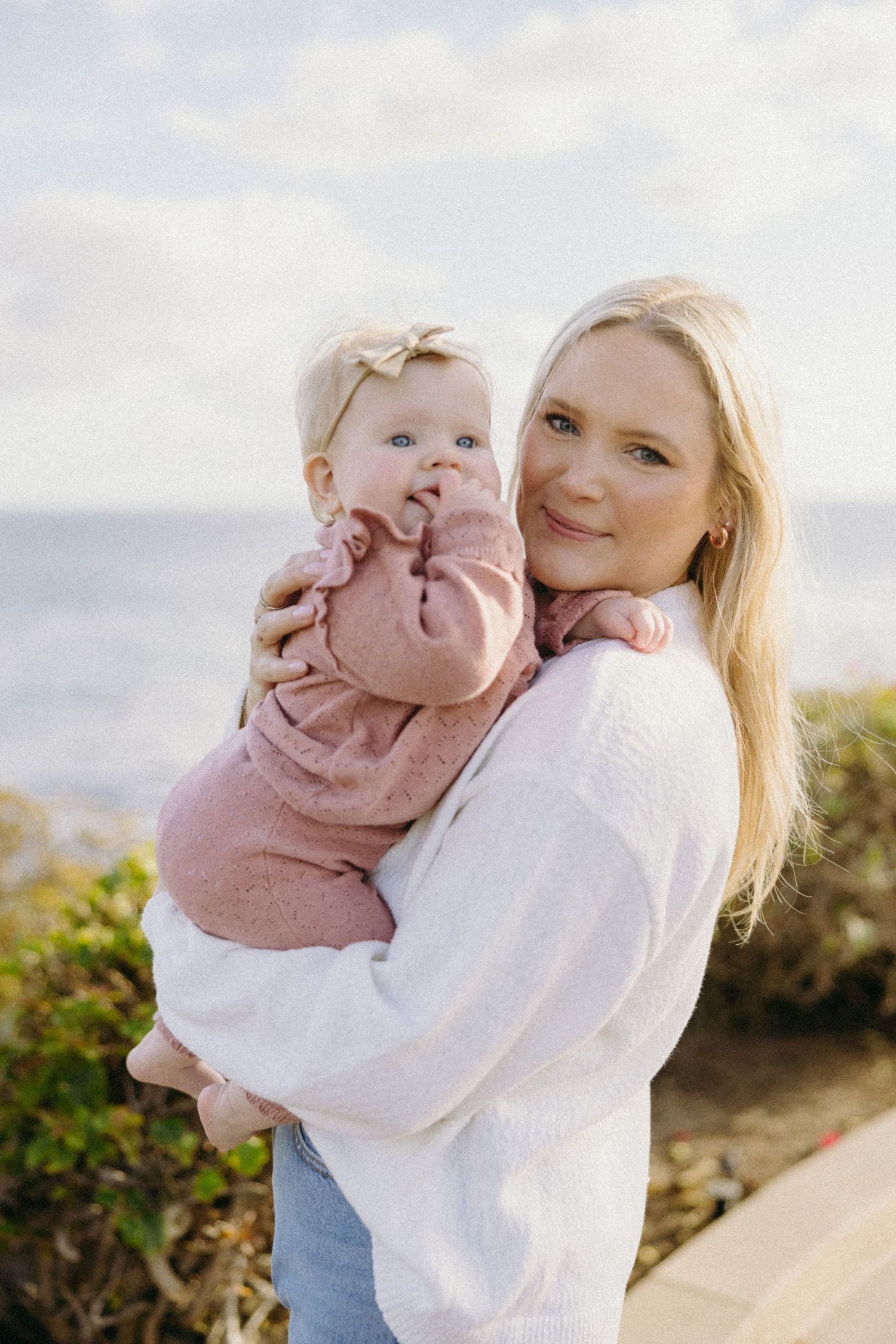 Mother and baby sharing joyful moments against a bright coastal backdrop.