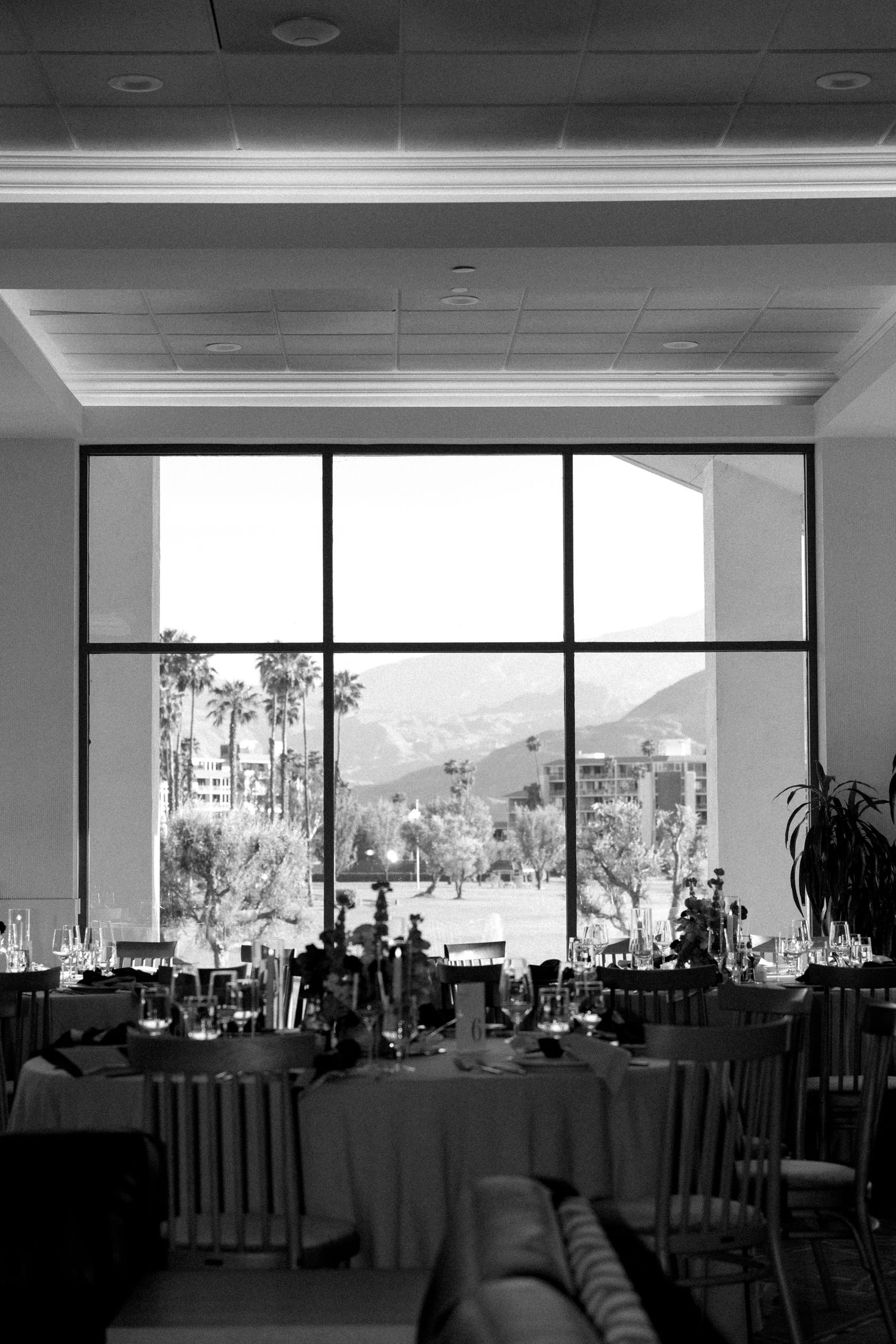 Black and white photo of an elegant banquet hall with mountain views through large windows and formally set dining tables.