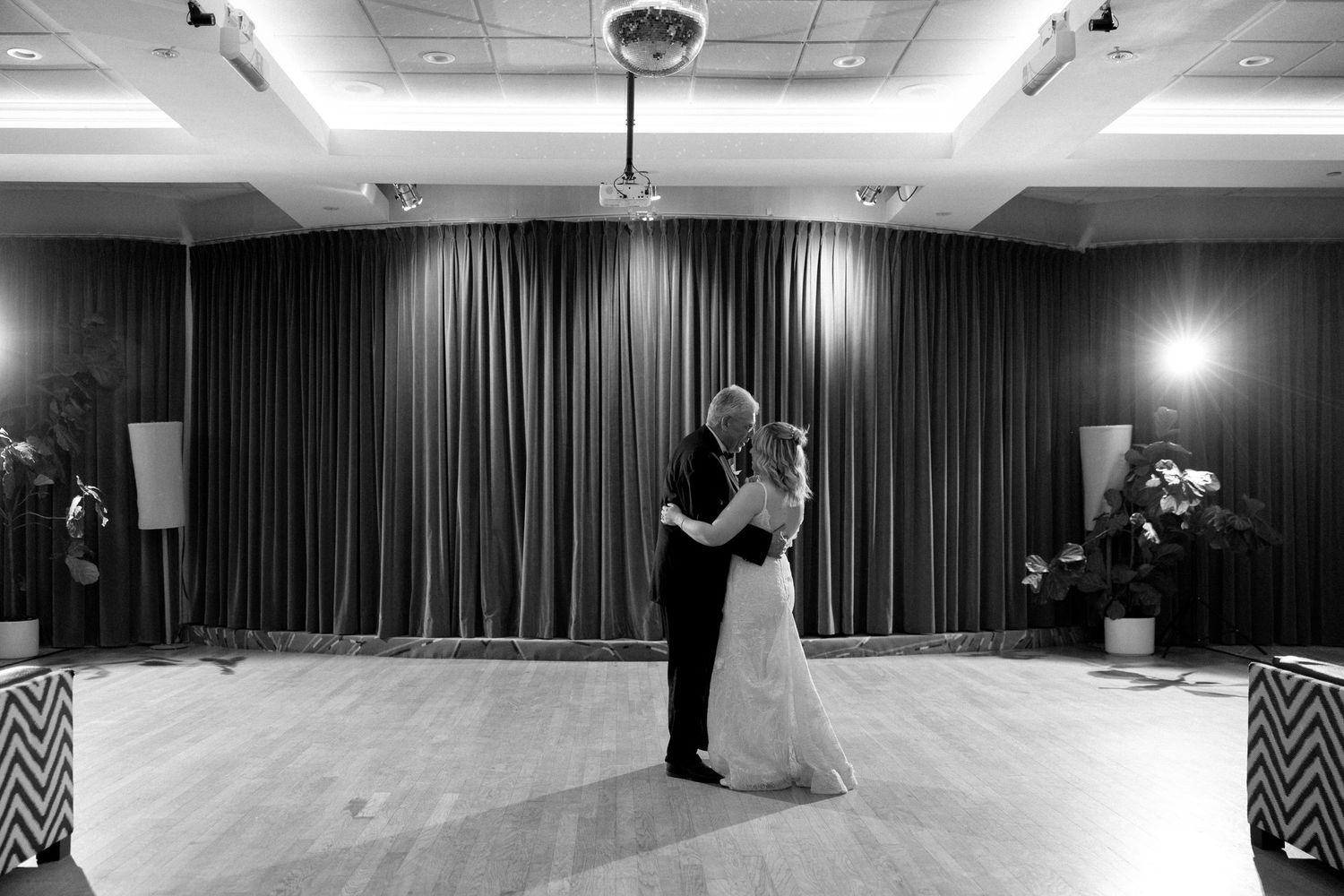 Black and white photo of a couple sharing their first dance at a wedding reception in an elegant ballroom.