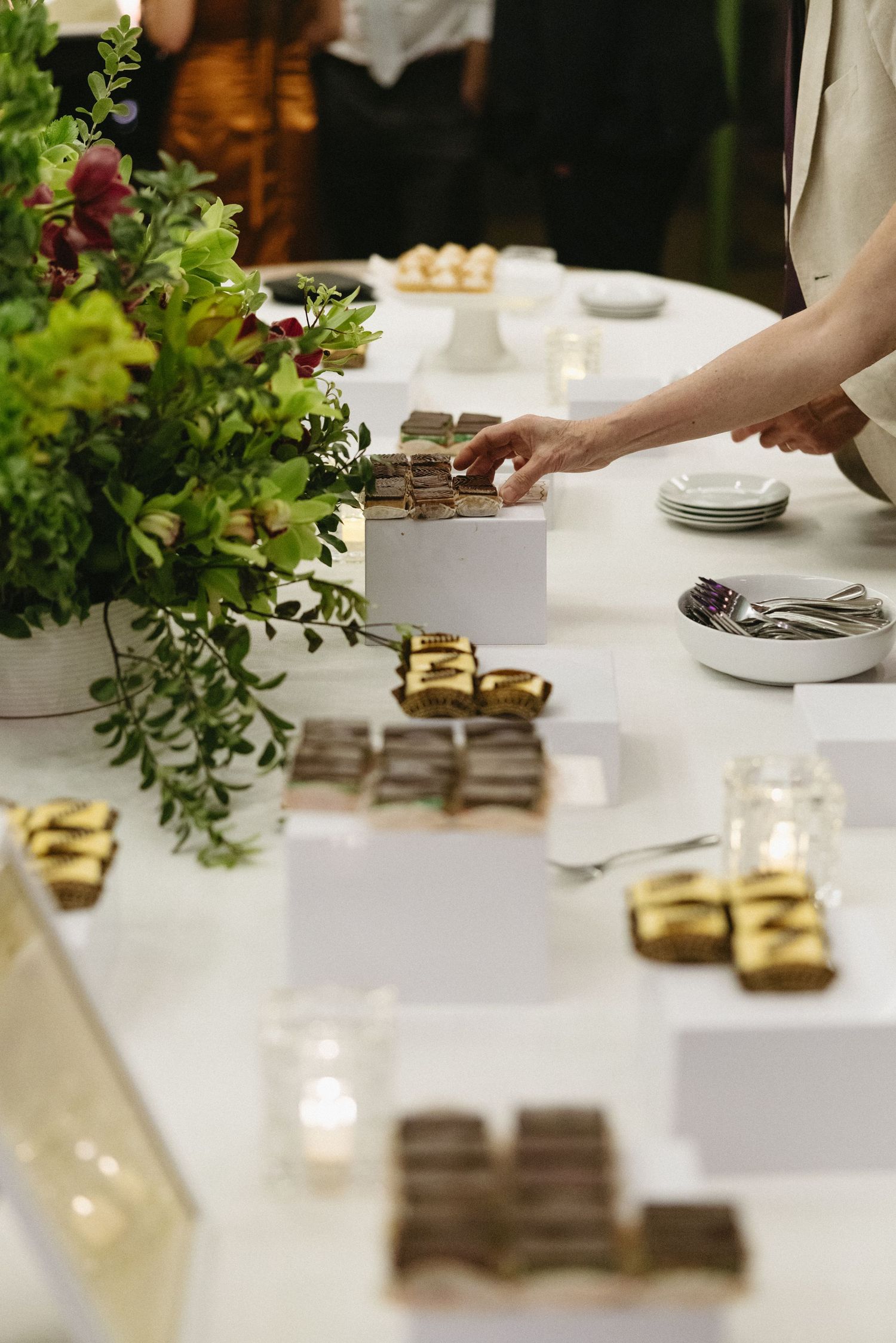 Elegant dessert table with chocolates, gold-wrapped sweets, floral centerpiece, and candles at a catered event.