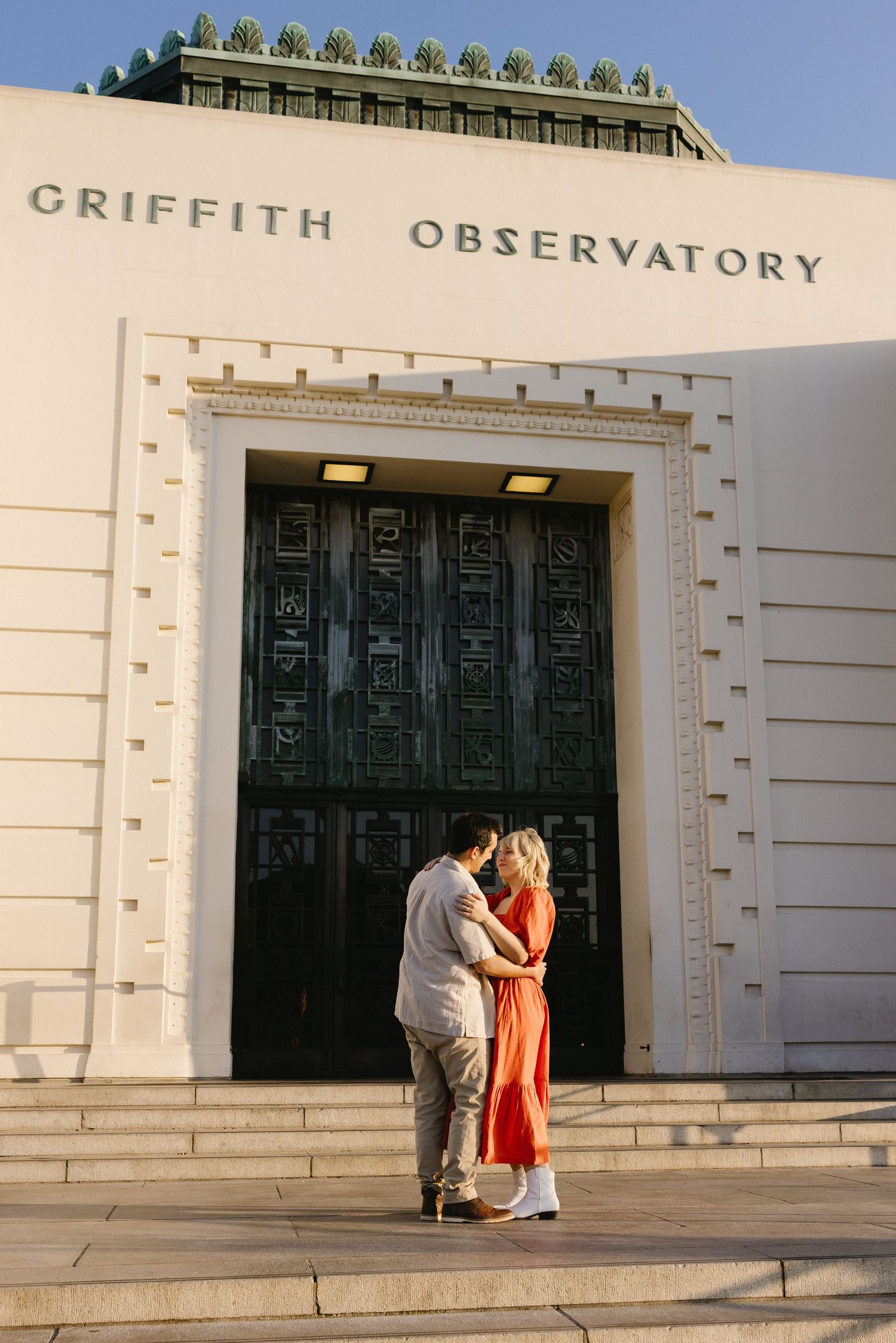 Couple sharing intimate moments outside the white facade of Griffith Observatory.