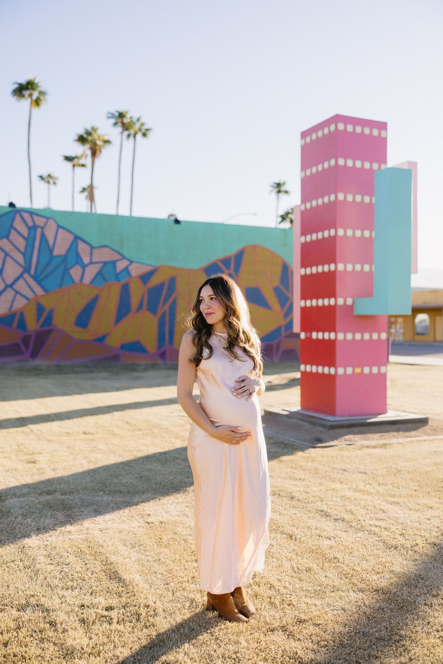 A maternity photoshoot in front of colorful geometric murals and palm trees at golden hour.