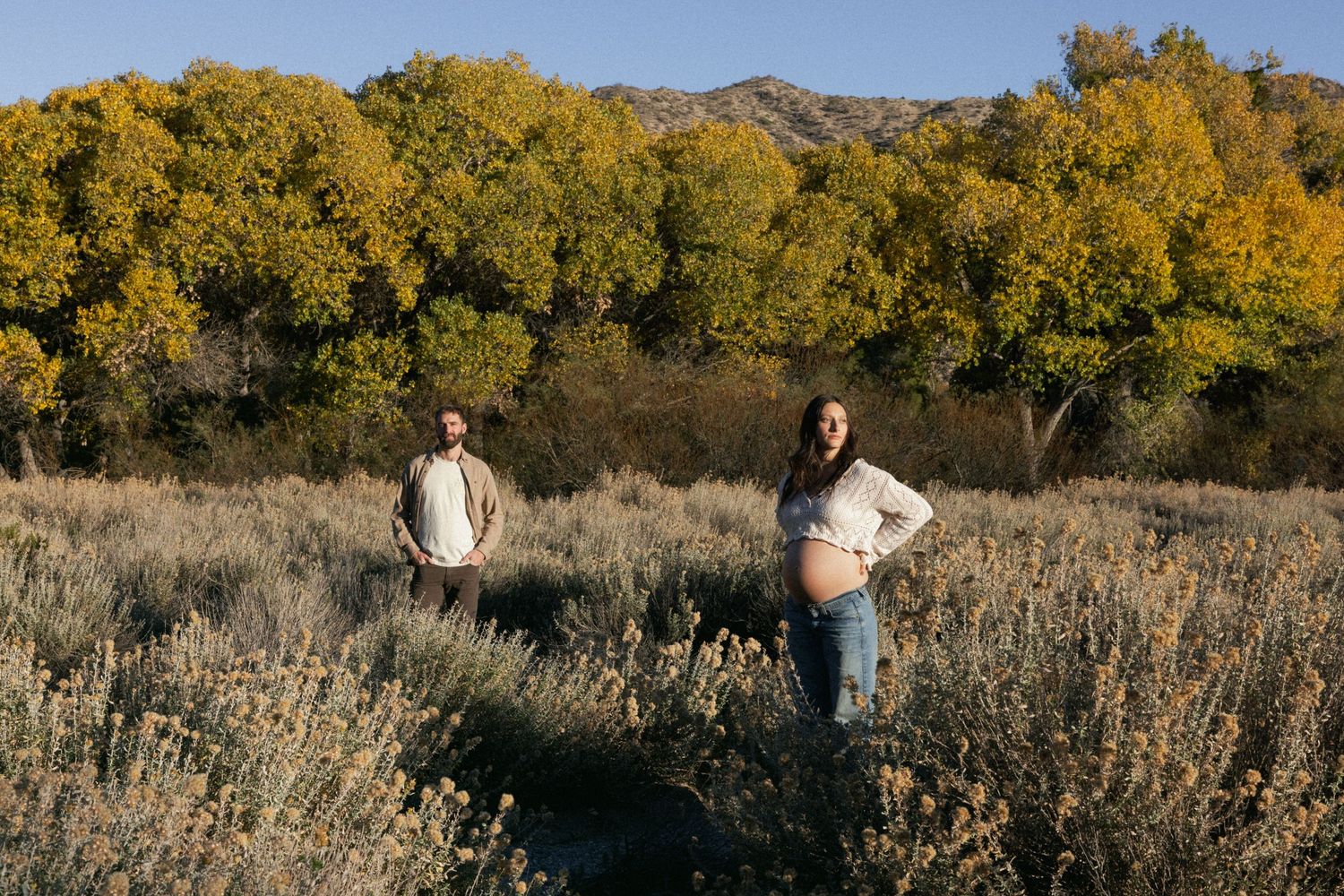 Two people pose in a desert landscape with golden autumn trees and mountains.
