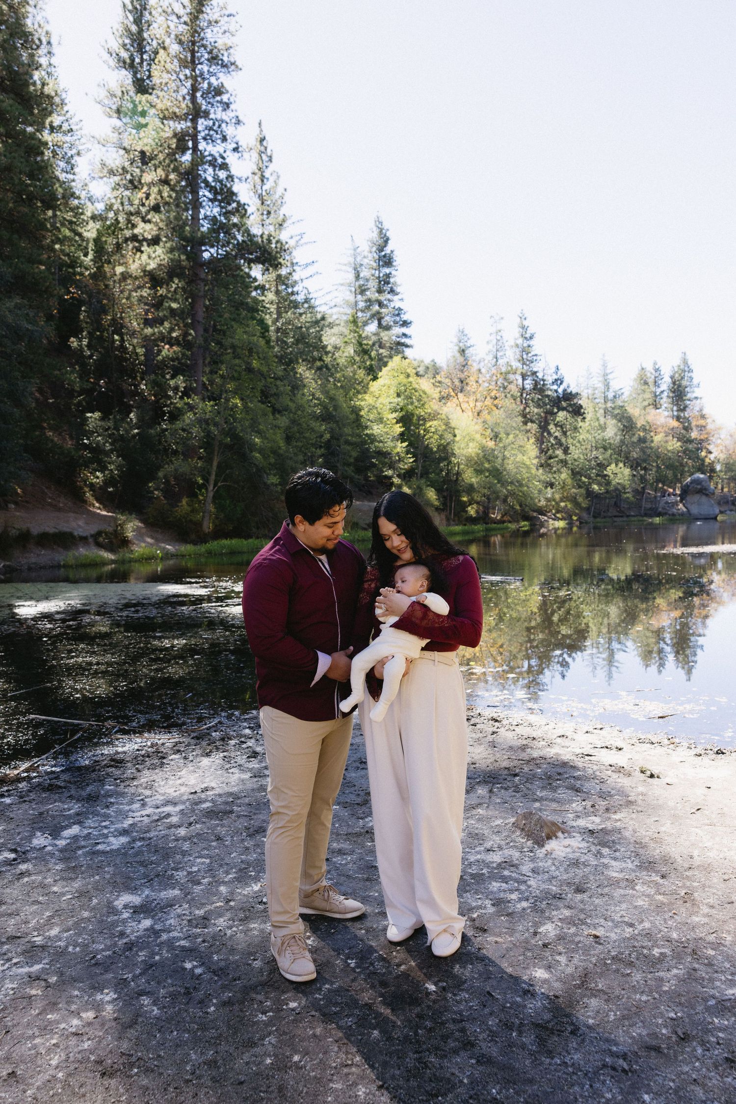 Family photo session by a tranquil lake with evergreen forest backdrop.