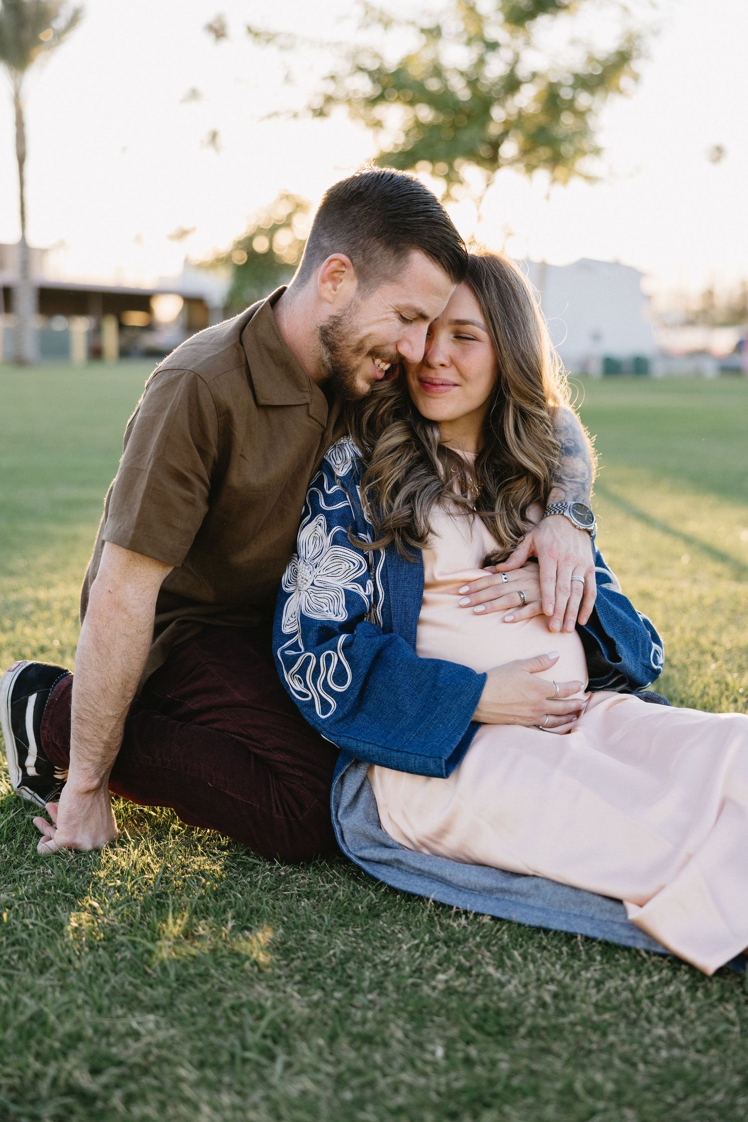 Intimate couple's maternity session on green grass during golden hour.