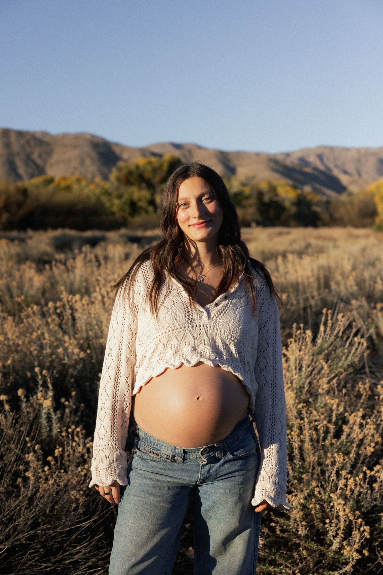 A maternity portrait in a desert setting with mountains and fall colors in the background.