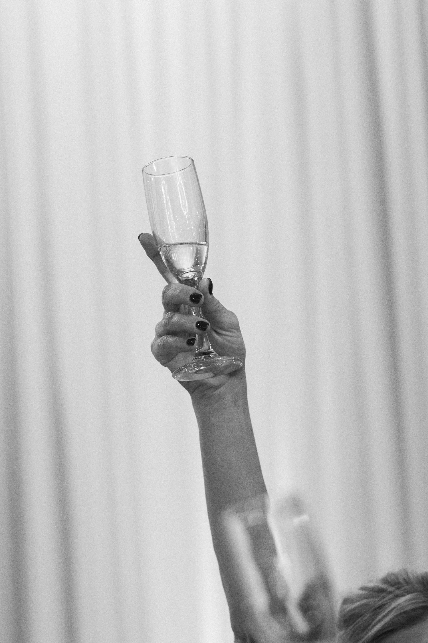 Black and white photo of a woman raising a champagne flute in celebration at a formal event.