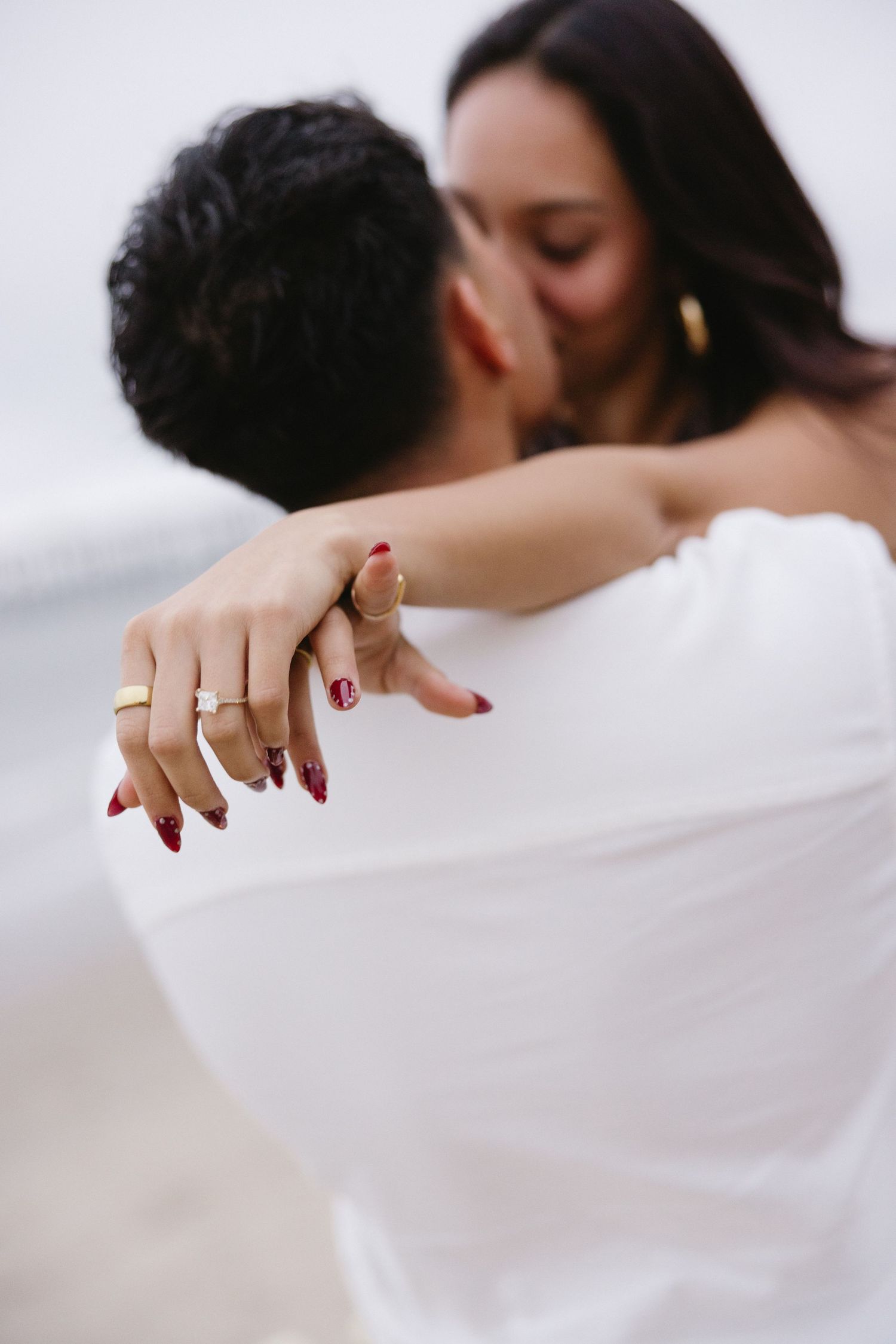 Romantic couple embracing in soft light with red nail polish detail.