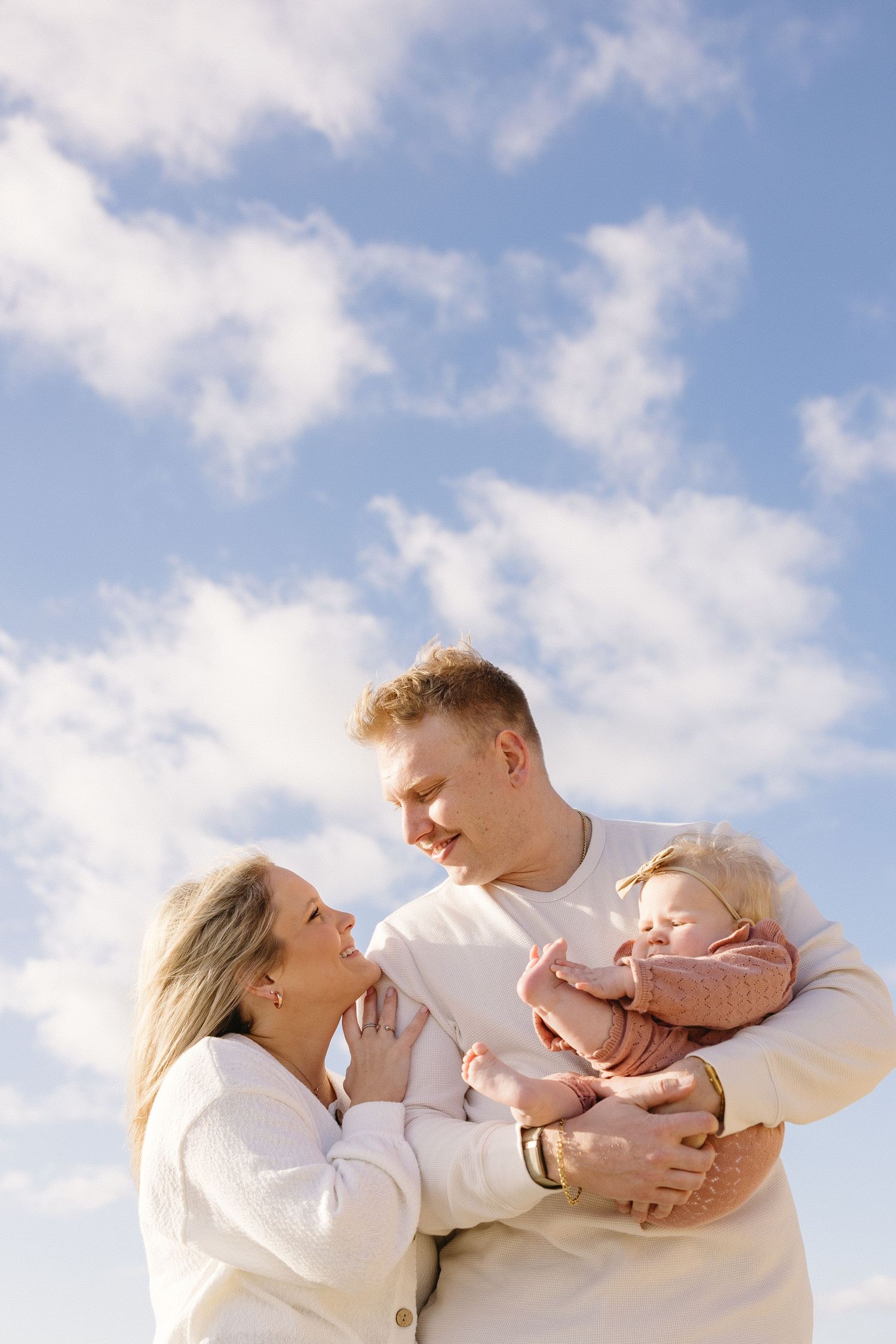Family embracing against blue sky and white clouds during outdoor photoshoot.