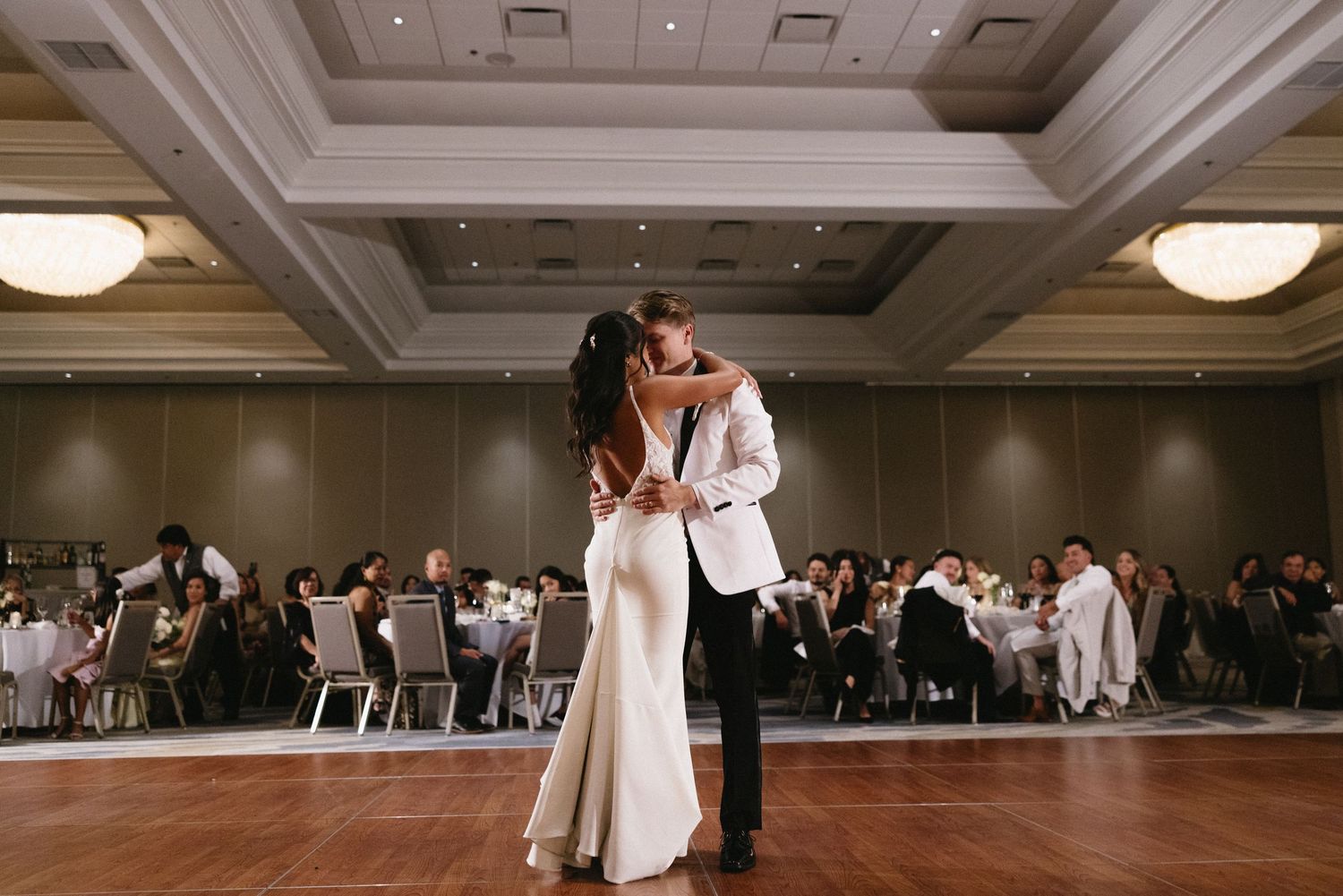 Wedding reception ballroom with guests watching first dance on wooden floor.