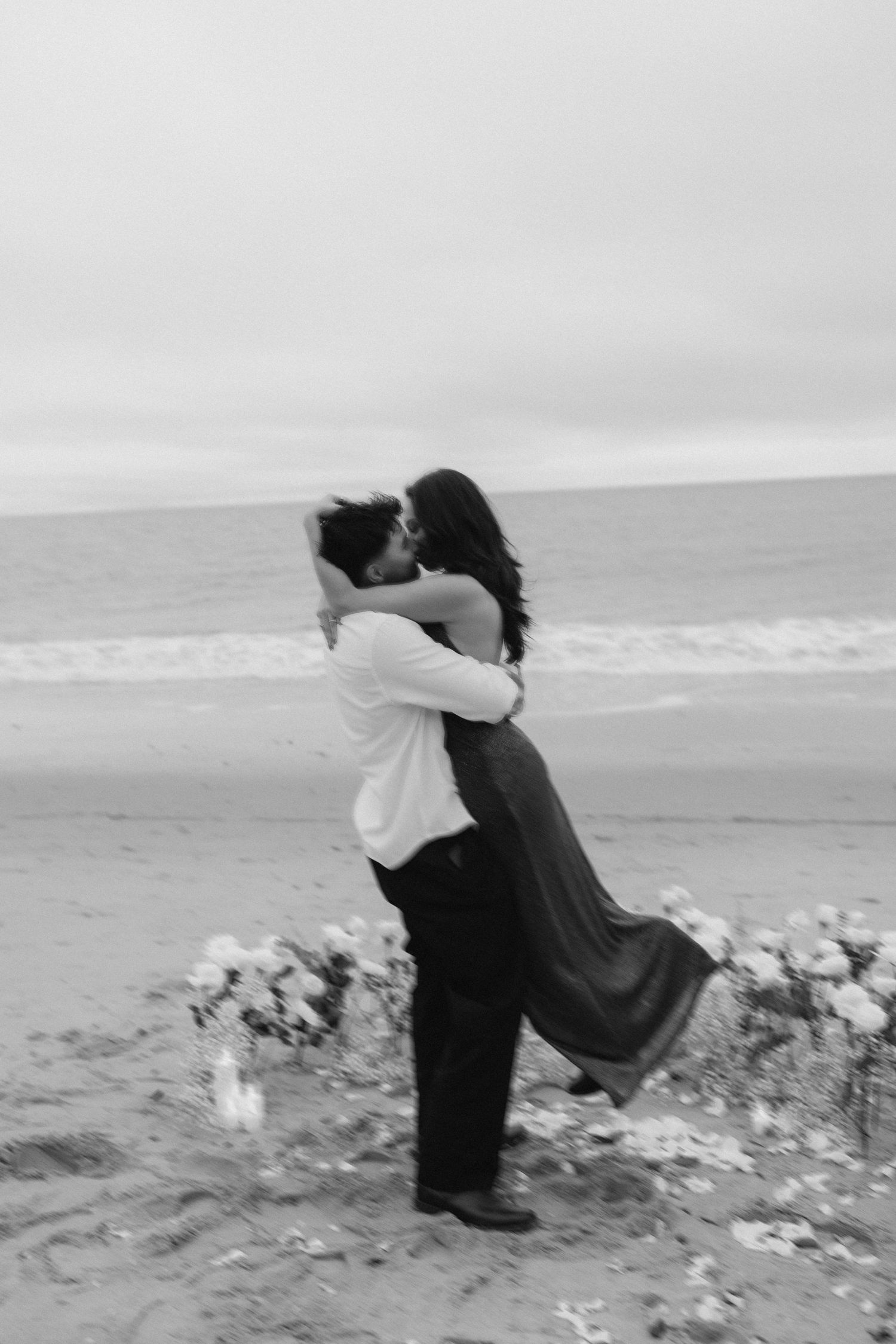 Joyful embrace on beach with ocean waves splashing in background.