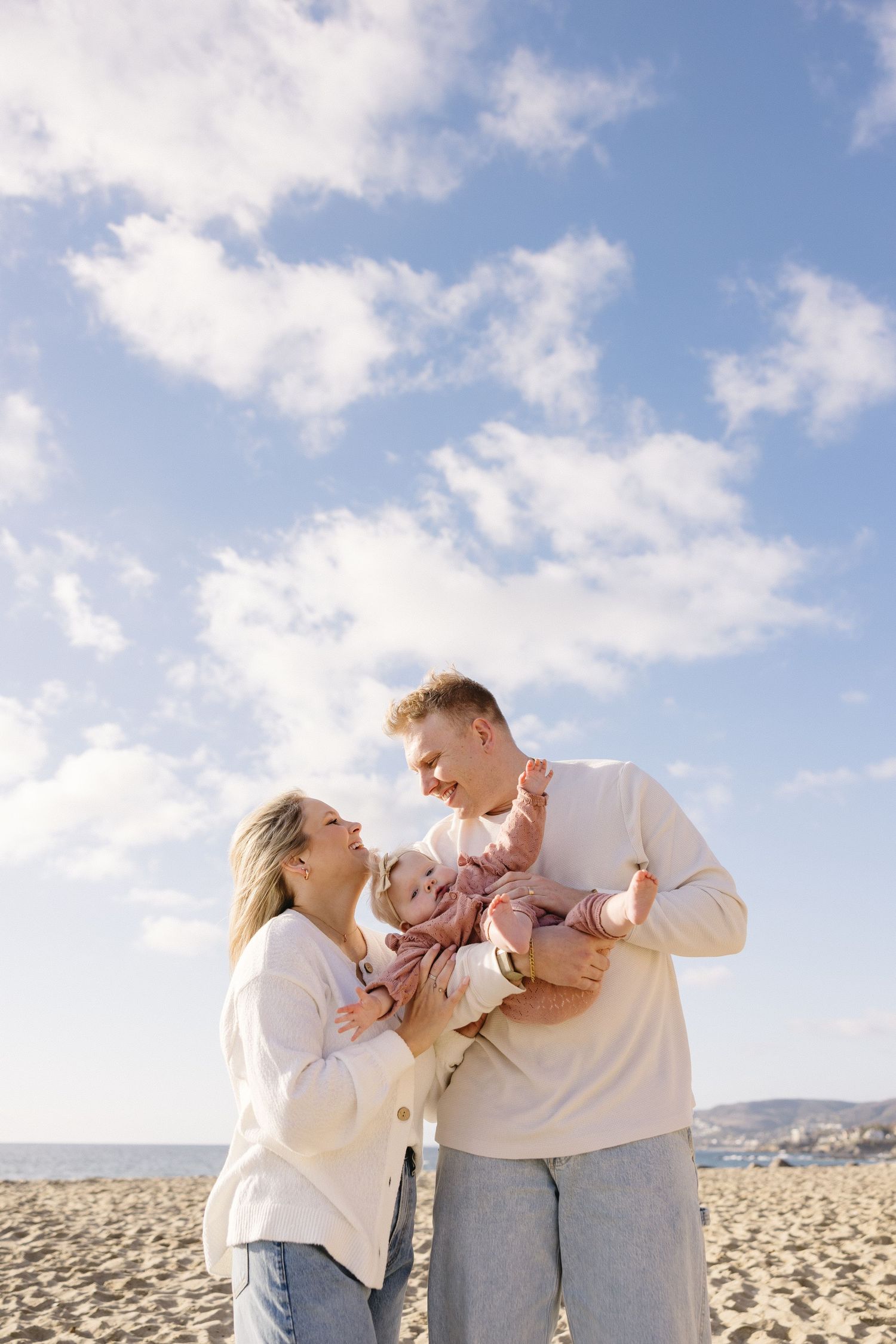 Family sharing intimate moments on a sandy beach under blue skies.