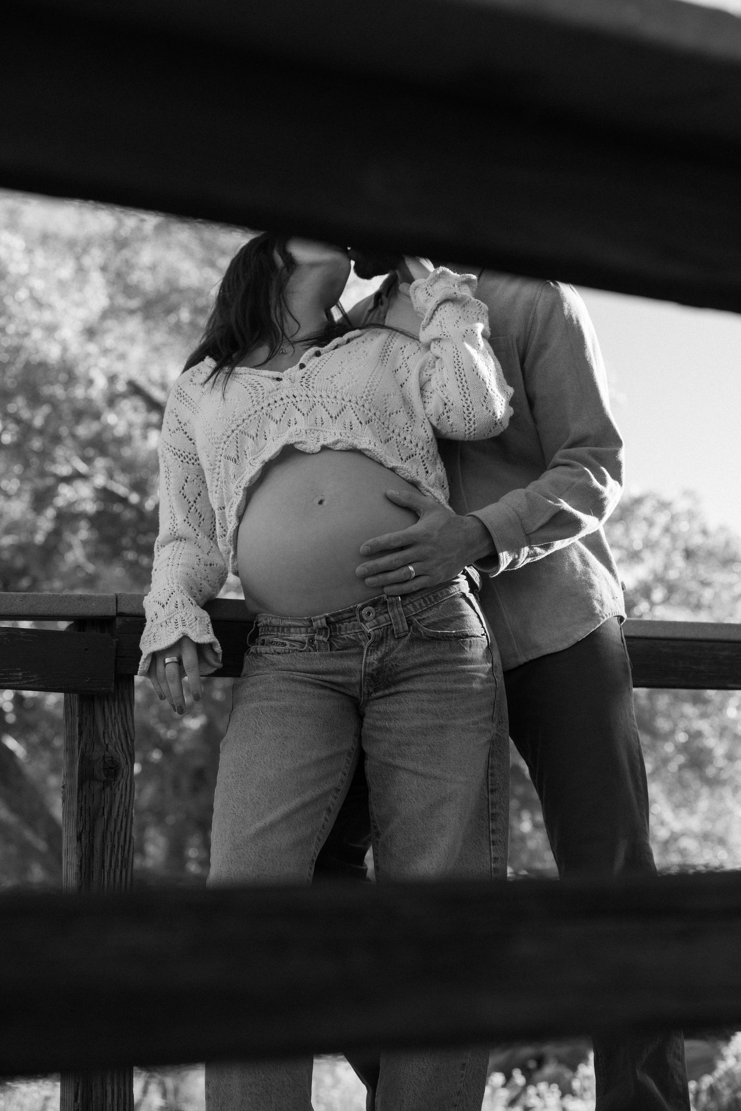Black and white photo capturing intimate moment between couple on wooden bridge.