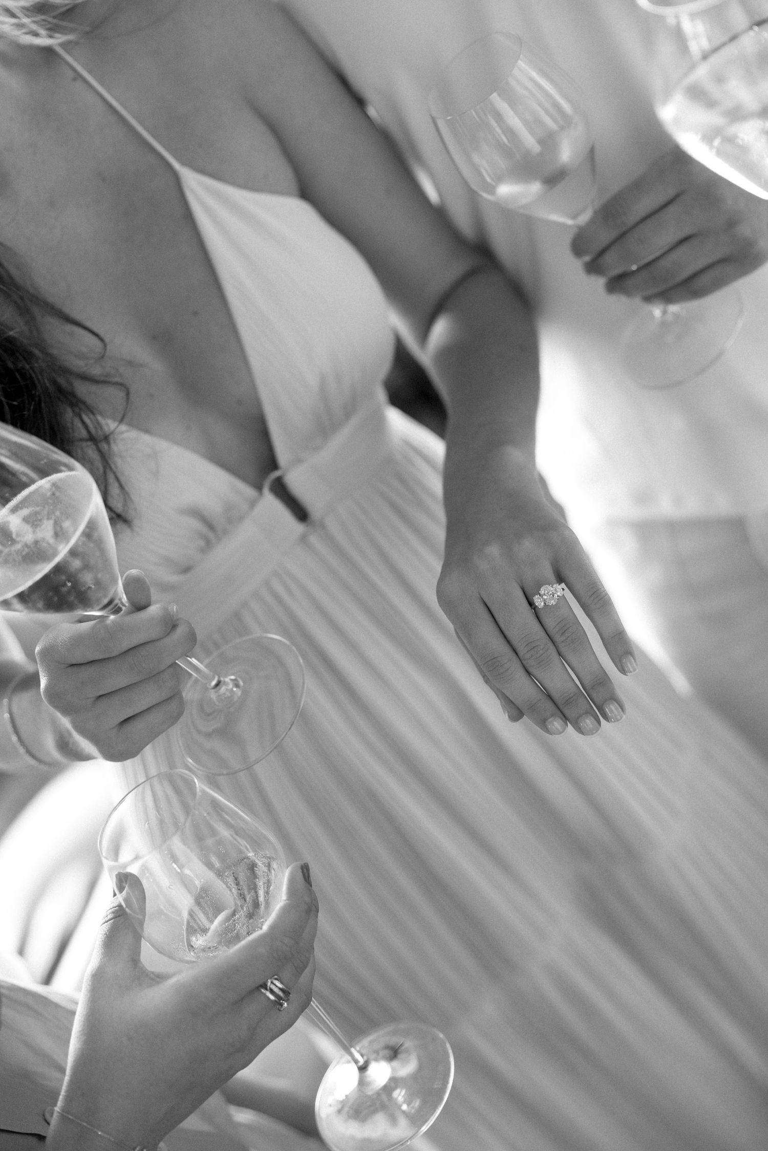 Black and white photo of women in elegant dresses holding wine glasses, one displaying a diamond engagement ring.