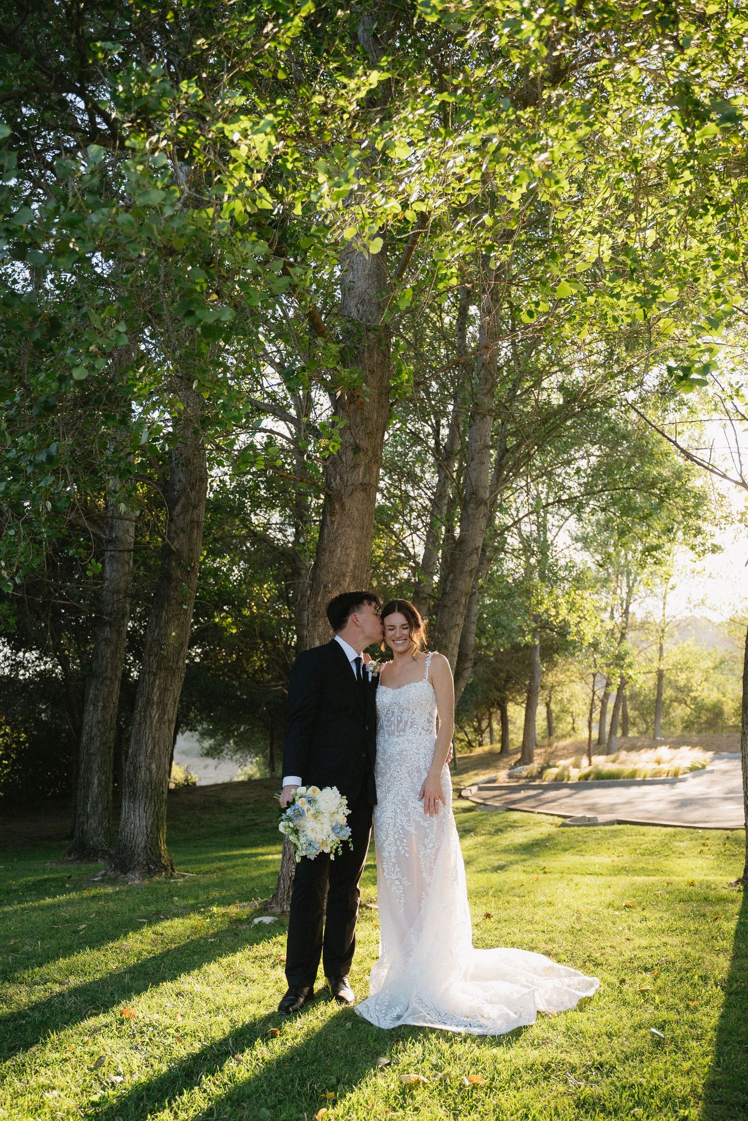 Wedding couple portraits in sunlit garden with beautiful green trees.