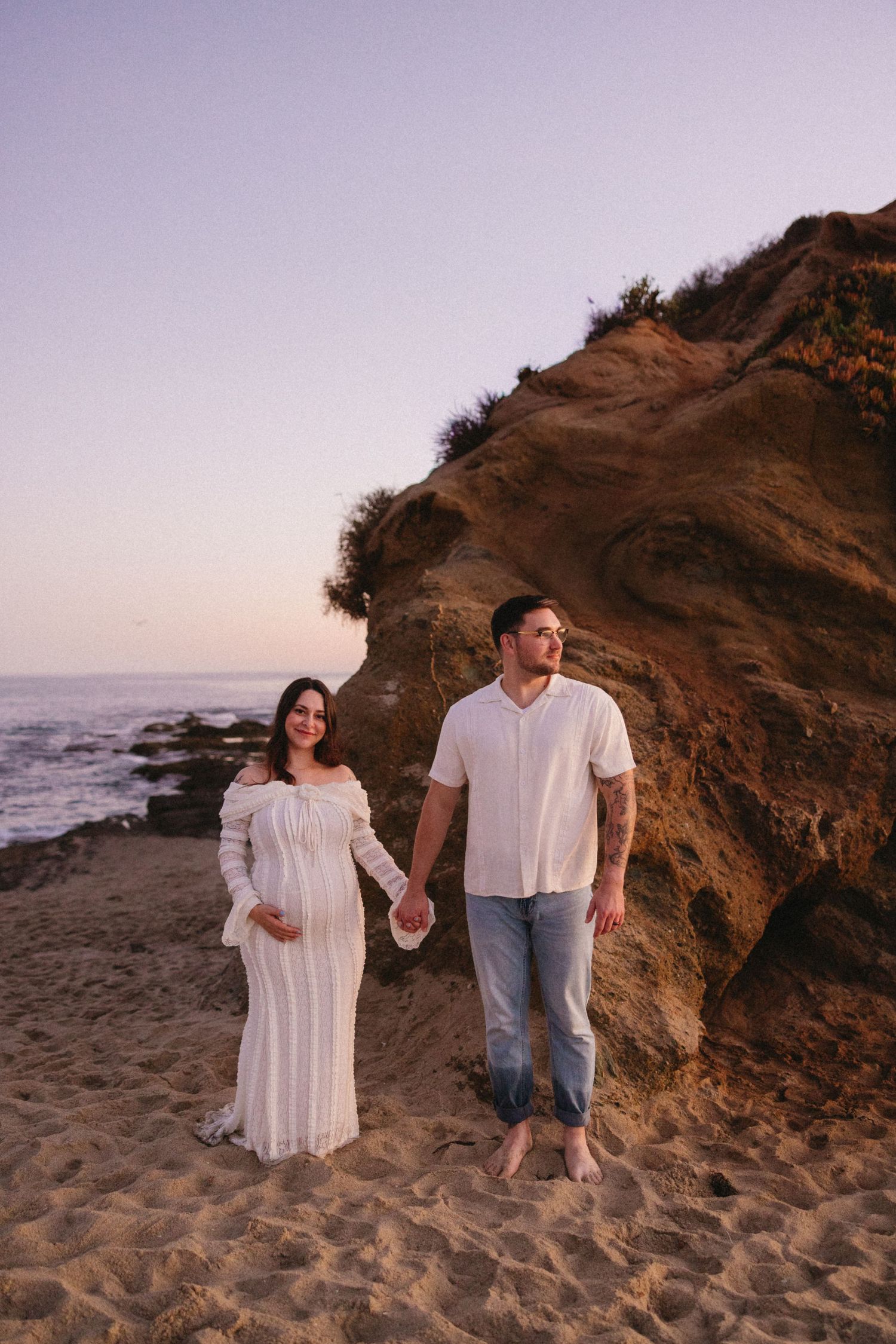 Couple holding hands near dramatic coastal cliffs at sunset.