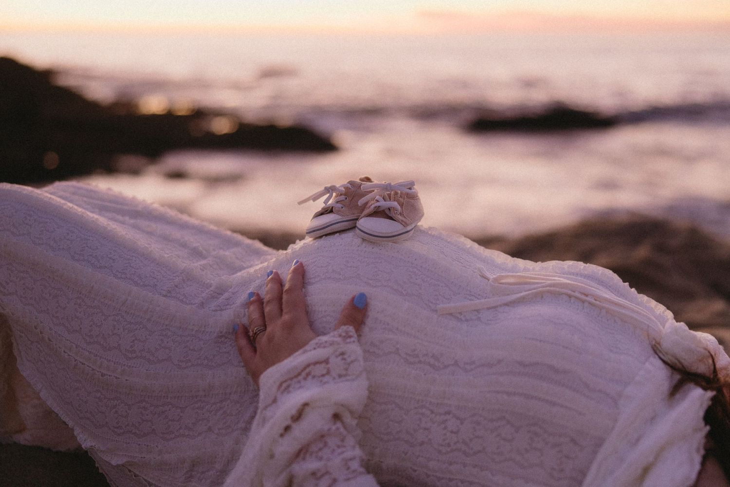 White lace wedding dress detail against sunset beach backdrop.