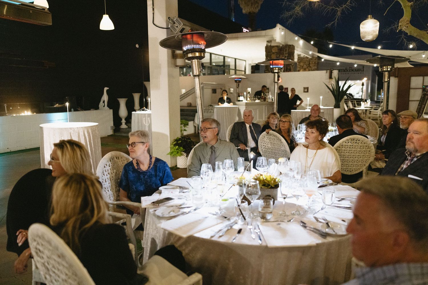 Guests seated at elegant round tables during a formal dinner event in a warmly lit venue.