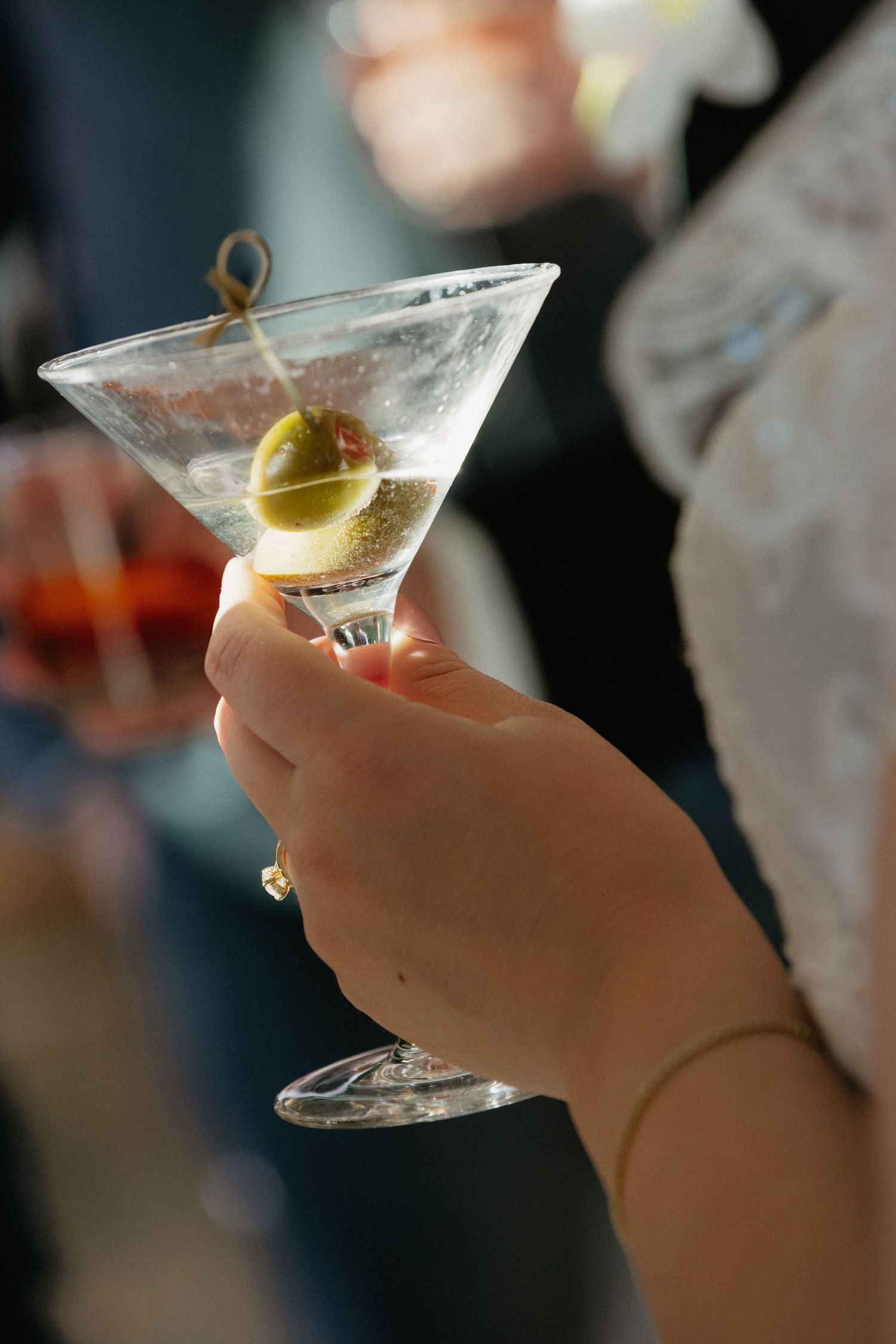 Hand holding a classic martini glass with olive garnish at an elegant wedding cocktail hour reception.